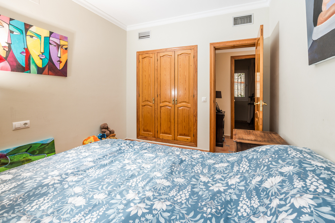 Dormitorio con armario empotrado de madera, paredes claras con arte moderno y cama vestida con textiles de motivos florales en tonos azules.