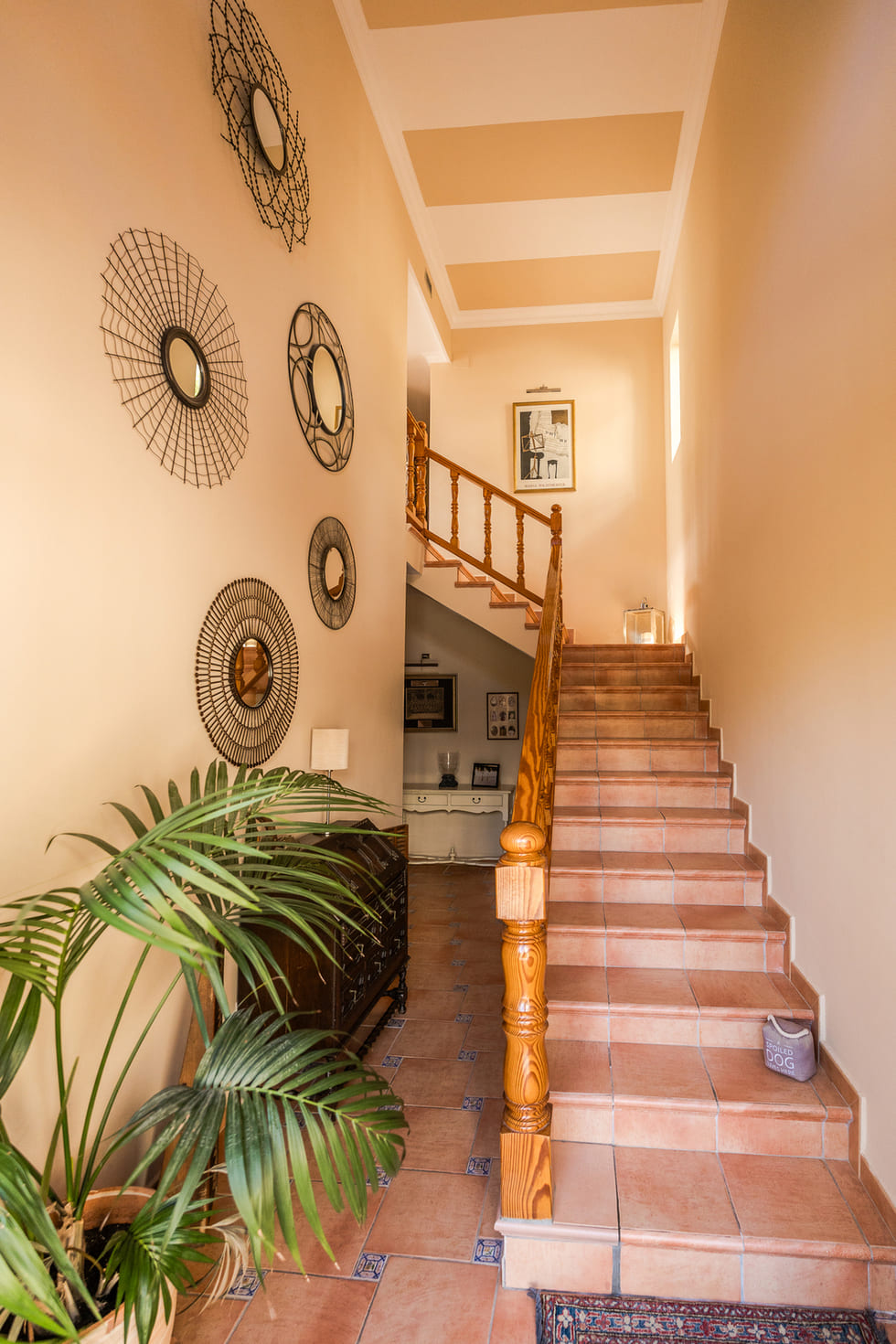 Hall de entrada con escalera de baldosas cerámicas, barandilla de madera, espejos decorativos de metal y techo con diseño de franjas.