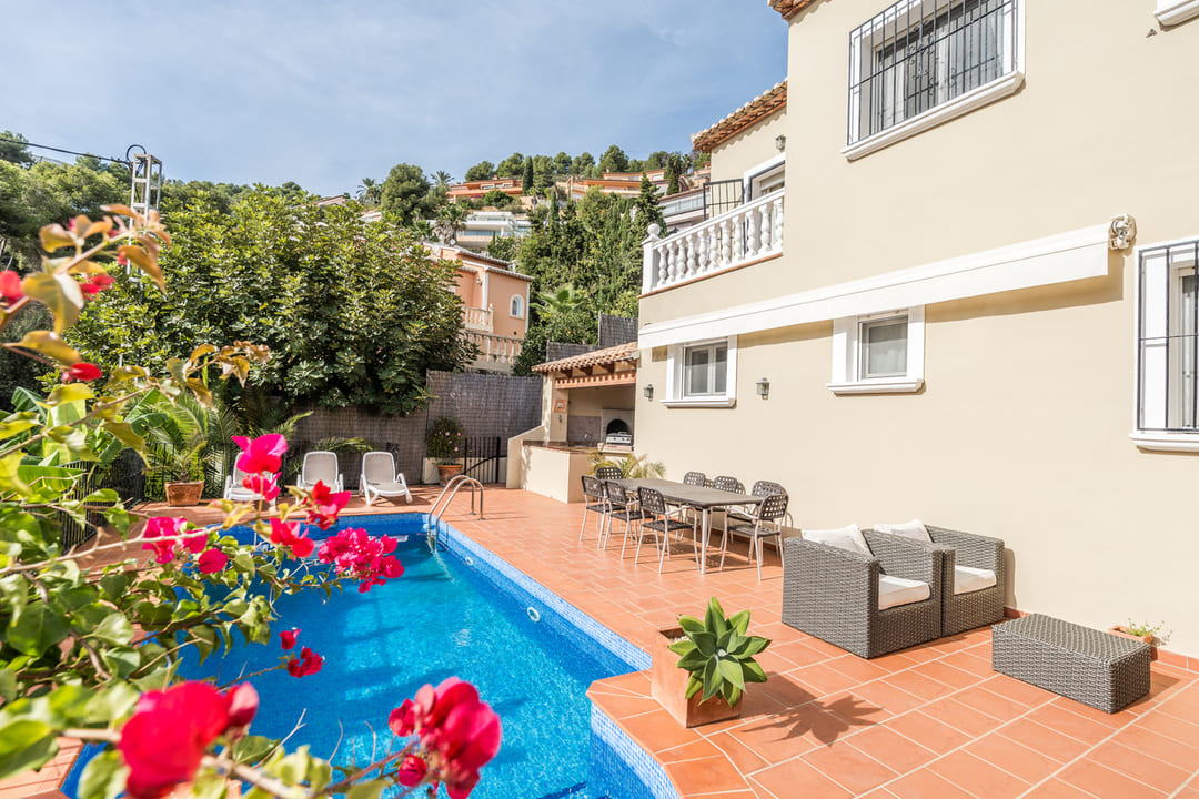 Terraza con piscina privada, suelo de terracota y zona de comedor exterior. Incluye barbacoa de obra y mobiliario de jardín junto a la fachada color crema.