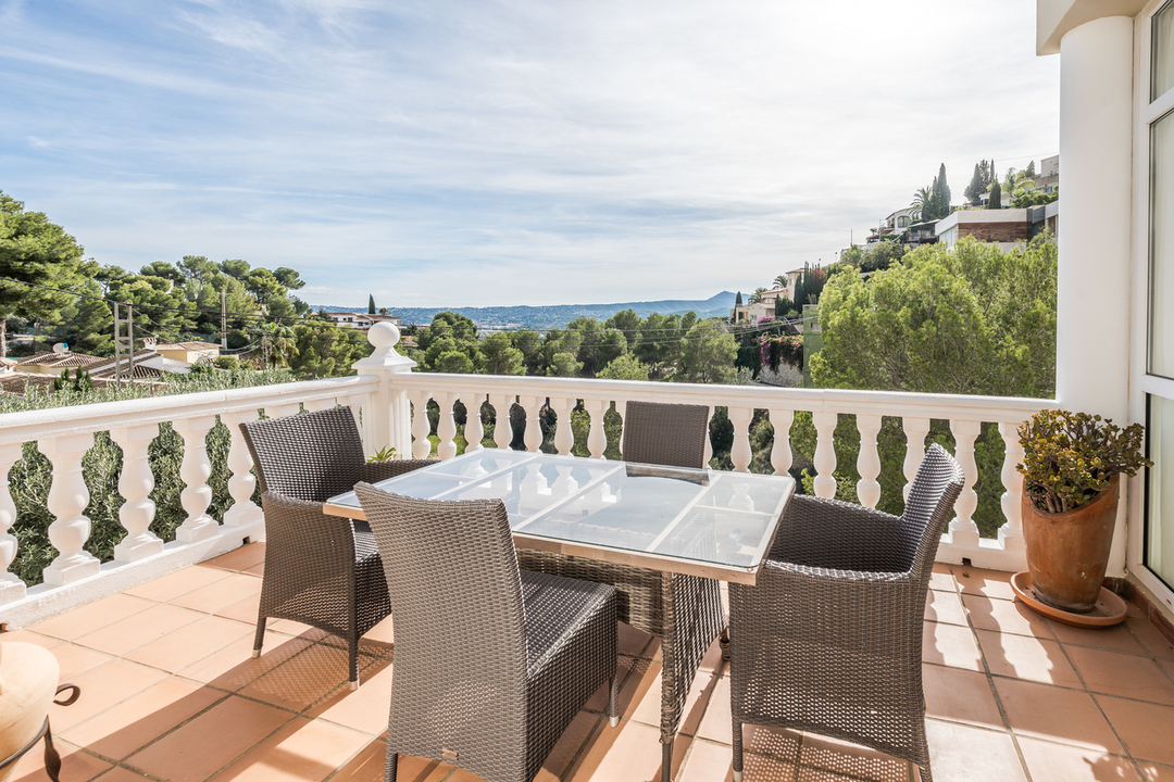 Terraza con suelo de terracota y balaustrada blanca, equipada con comedor de mimbre y vistas despejadas al valle y las montañas circundantes.