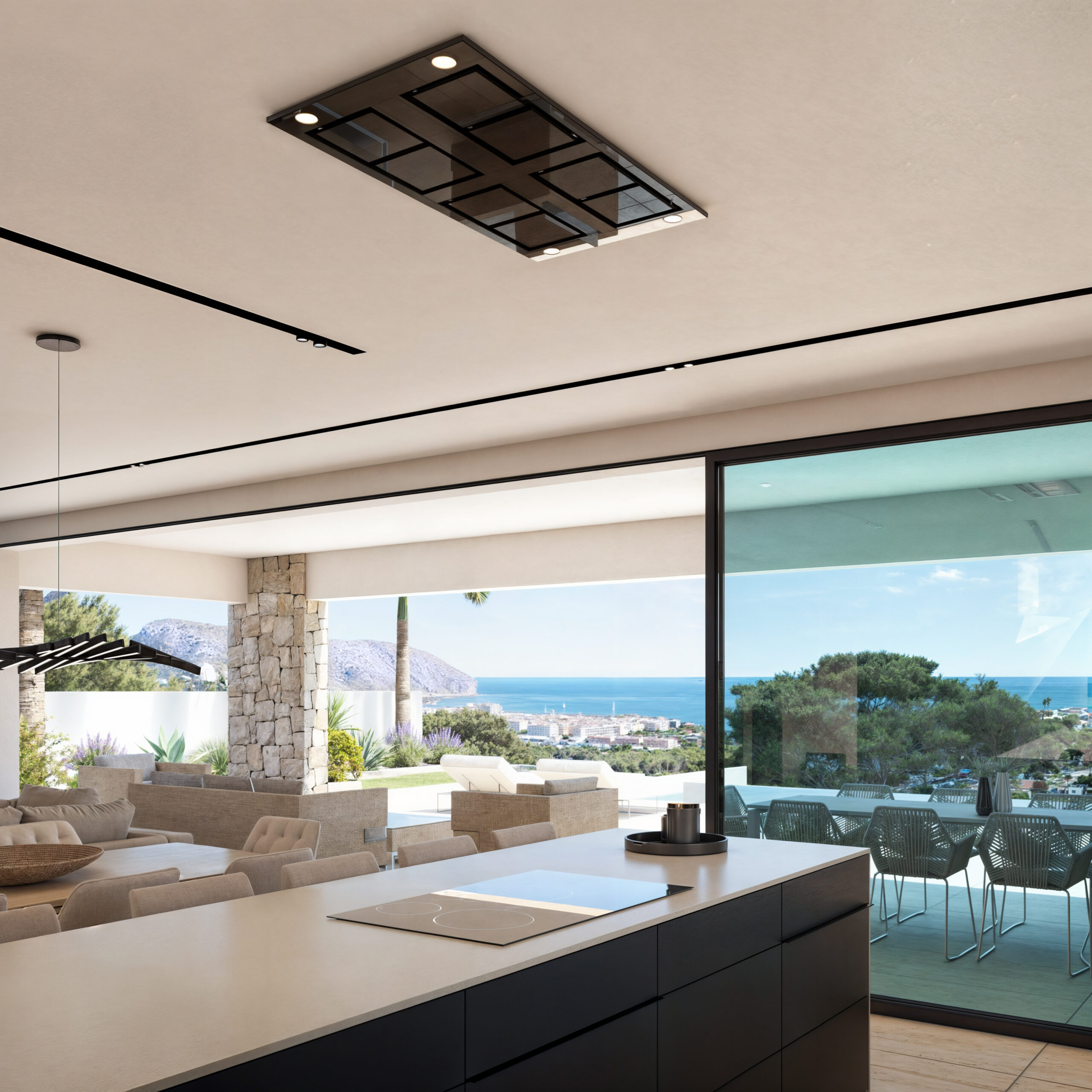 Isla de cocina con placa de inducción y campana integrada en el techo, abierta a una estancia con vistas al mar y terraza mediterránea.