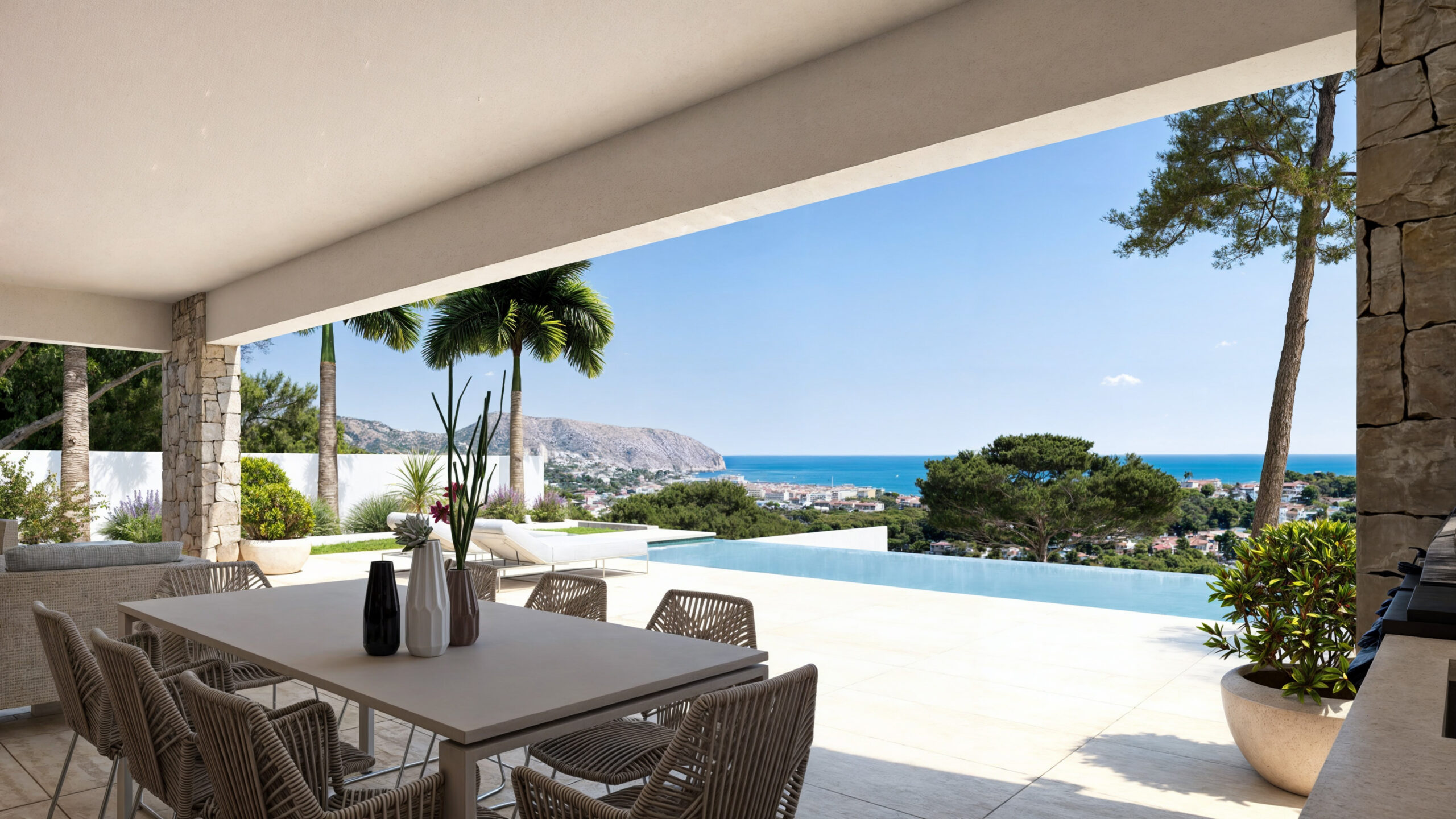 Terraza cubierta con comedor exterior, pilares de piedra natural y piscina infinita con vistas panorámicas al mar Mediterráneo y al paisaje costero.
