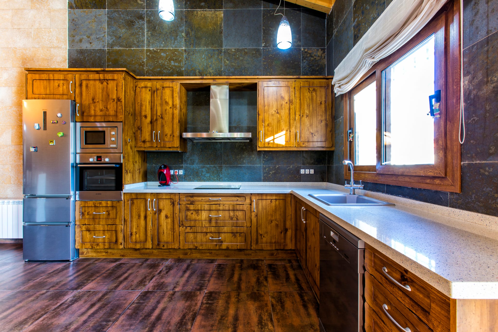 Cocina rústica con armarios de madera natural, paredes revestidas en piedra oscura y encimera de cuarzo claro, equipada con electrodomésticos de acero inoxidable.