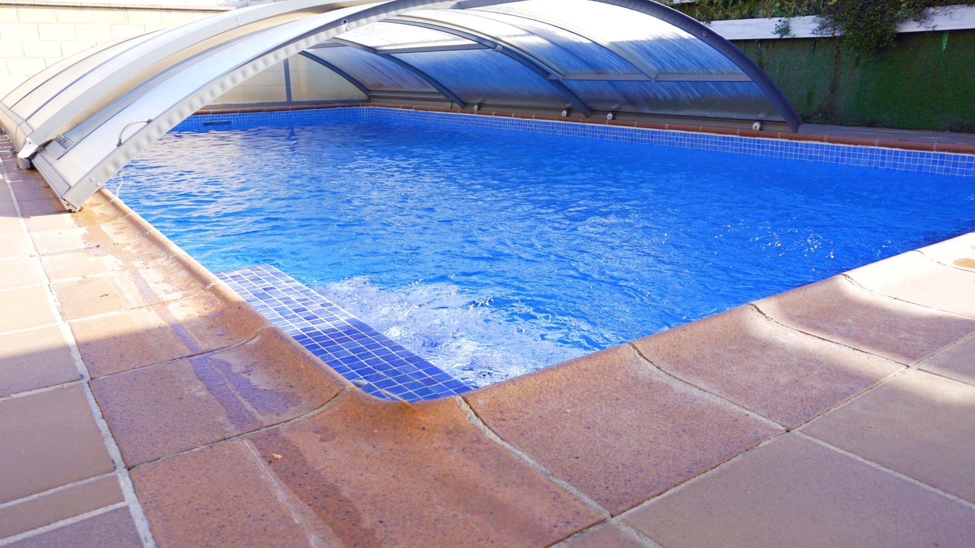 Piscina exterior con cubierta telescópica retráctil, revestimiento de gresite azul y coronación de piedra en tonos terracota.