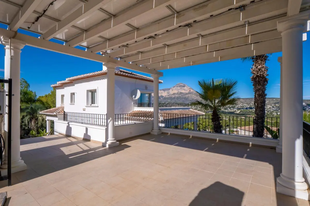 Amplia terraza cubierta con columnas blancas y pérgola, con vistas despejadas al monte Montgó y al paisaje mediterráneo circundante.