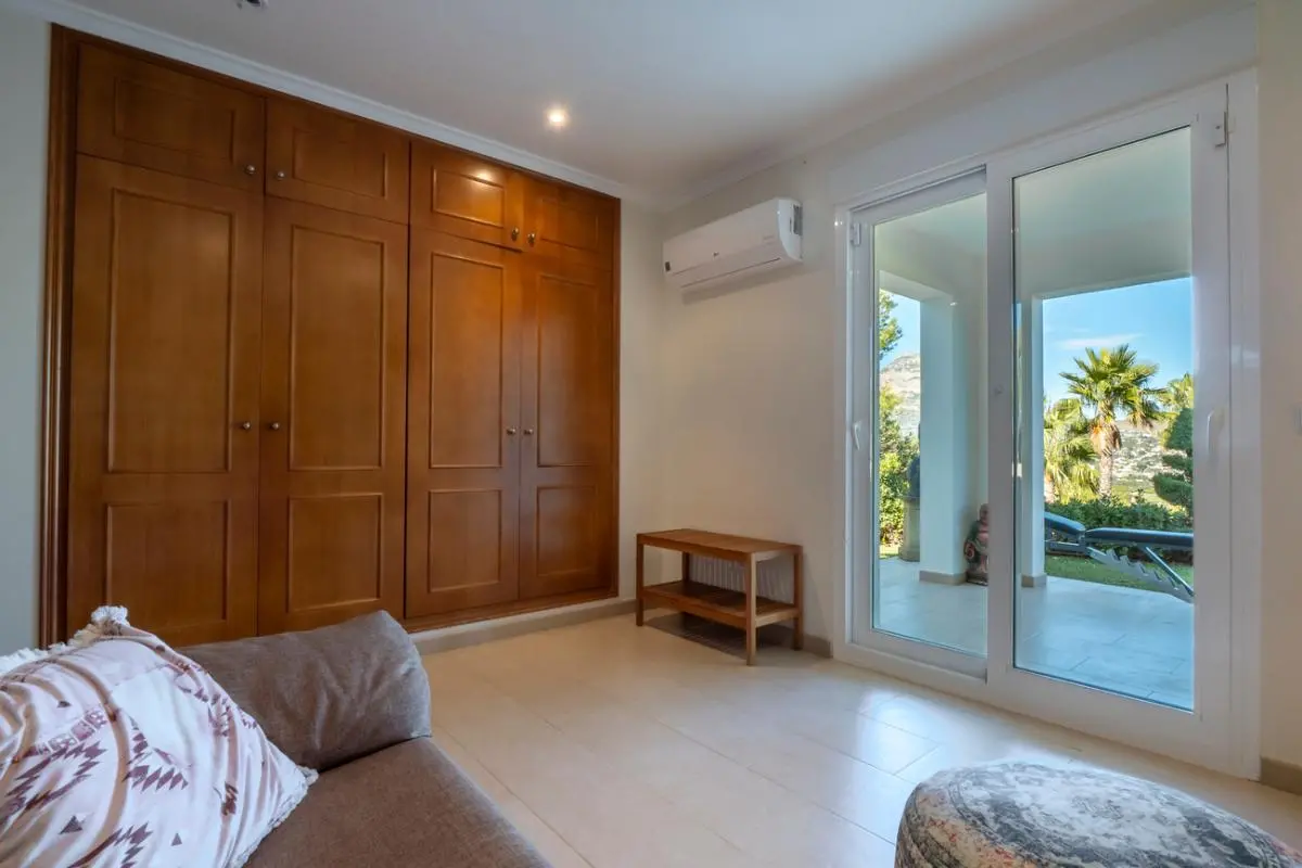 Dormitorio con armario empotrado de madera, aire acondicionado y puertas correderas de cristal con acceso a una terraza y vistas al jardín.