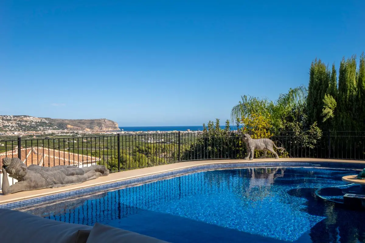 Piscina exterior con gresite azul, estatuas decorativas de piedra y vistas panorámicas hacia la costa mediterránea y el valle circundante.