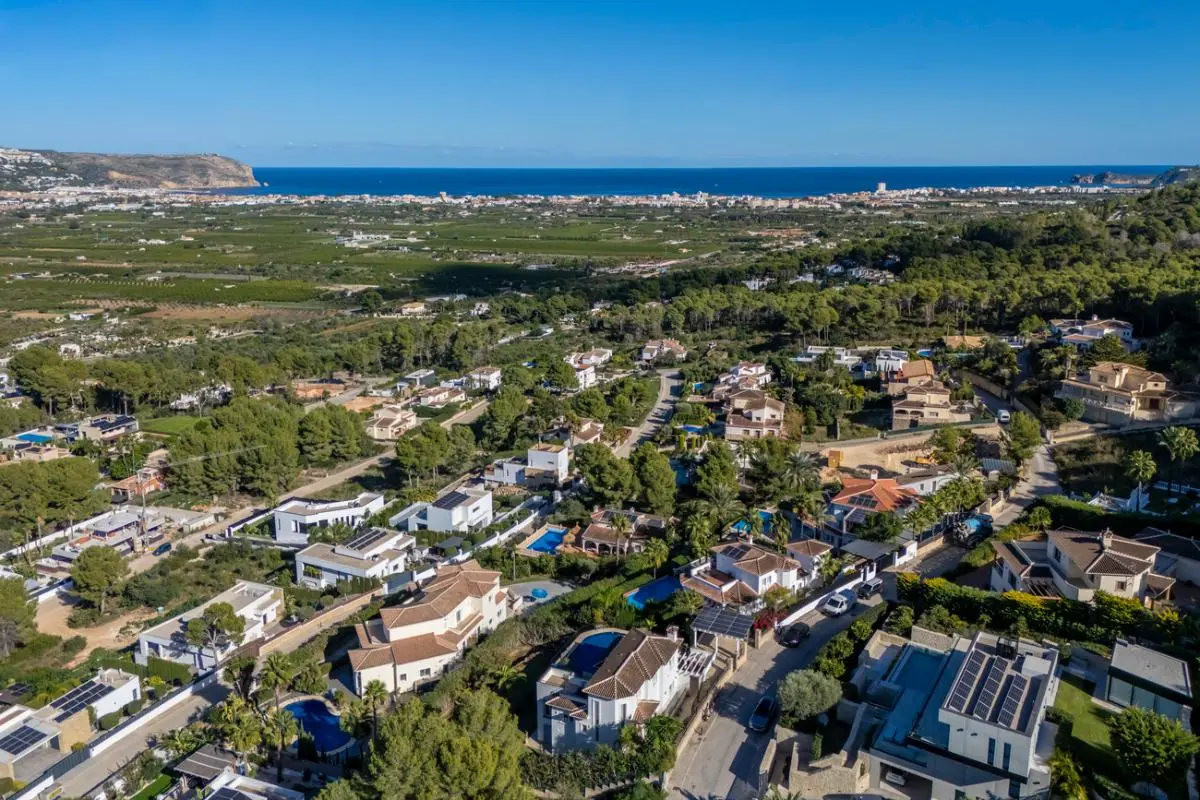 Vista aérea de una urbanización elevada con villas independientes, piscinas privadas y placas solares, orientada hacia el valle y la costa mediterránea.