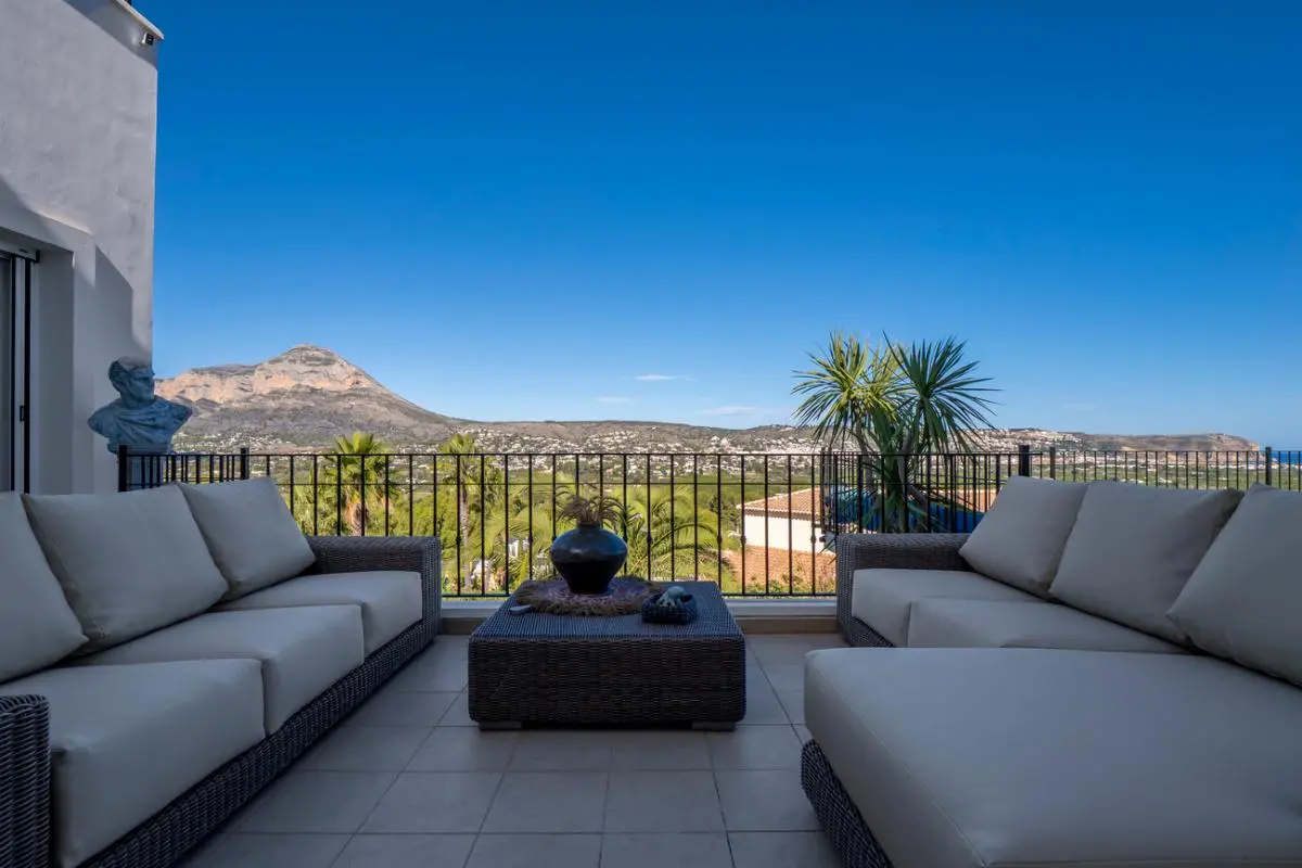 Zona de estar en terraza con sofás de mimbre gris y vistas panorámicas frontales al Montgó y al valle circundante.
