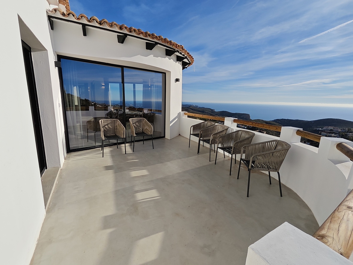 Amplia terraza curva con suelo de microcemento, asientos de cuerda trenzada y vistas panorámicas al Mediterráneo bajo una fachada blanca tradicional.