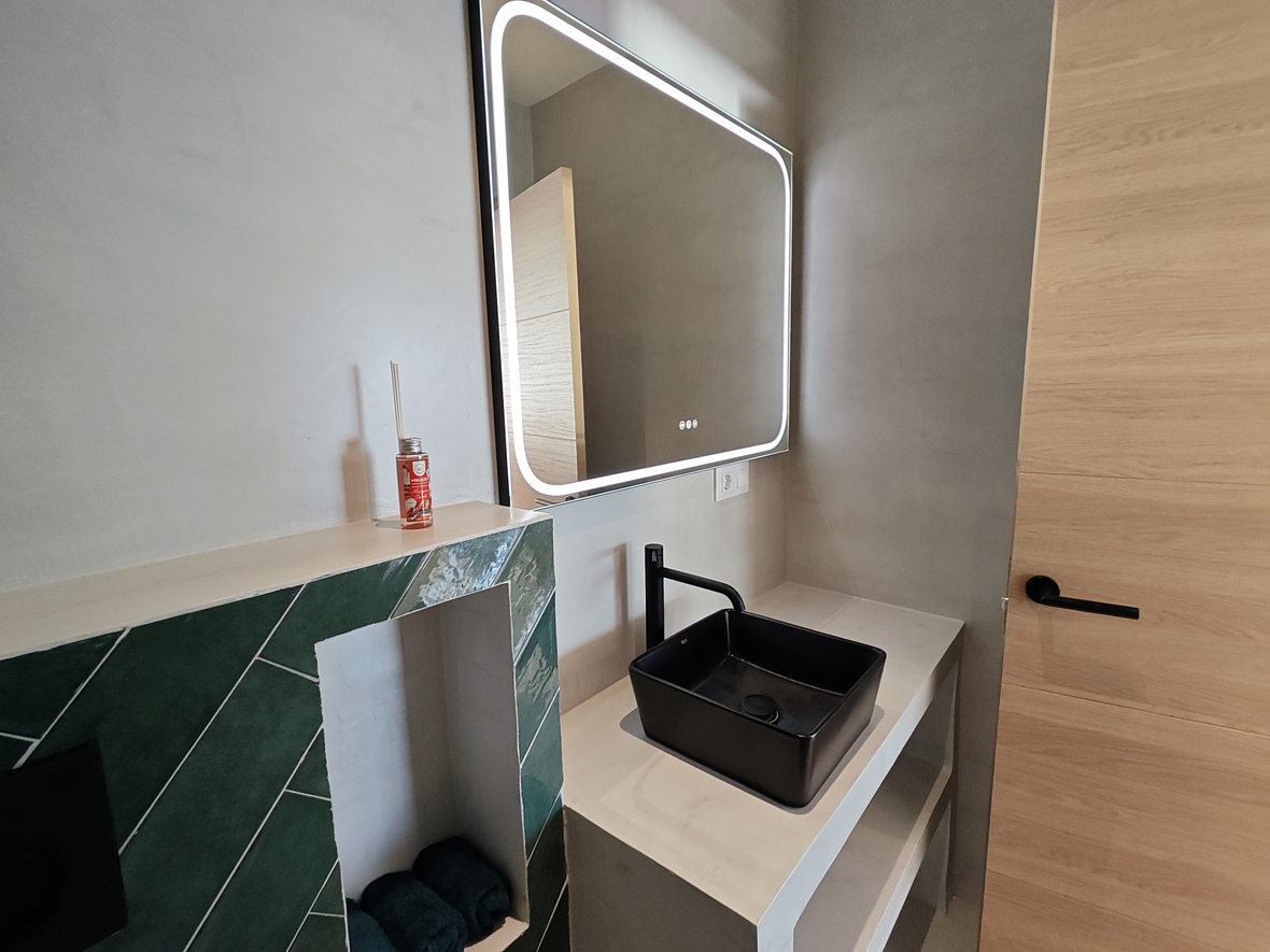 Baño contemporáneo con lavabo de diseño en color negro, espejo con iluminación LED integrada y revestimiento de azulejos verdes en espiga.