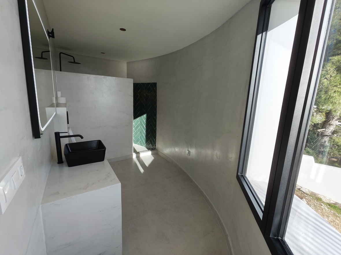 Baño de diseño minimalista con paredes curvas de microcemento, lavabo negro sobre encimera y ducha con azulejos verdes en espiga.