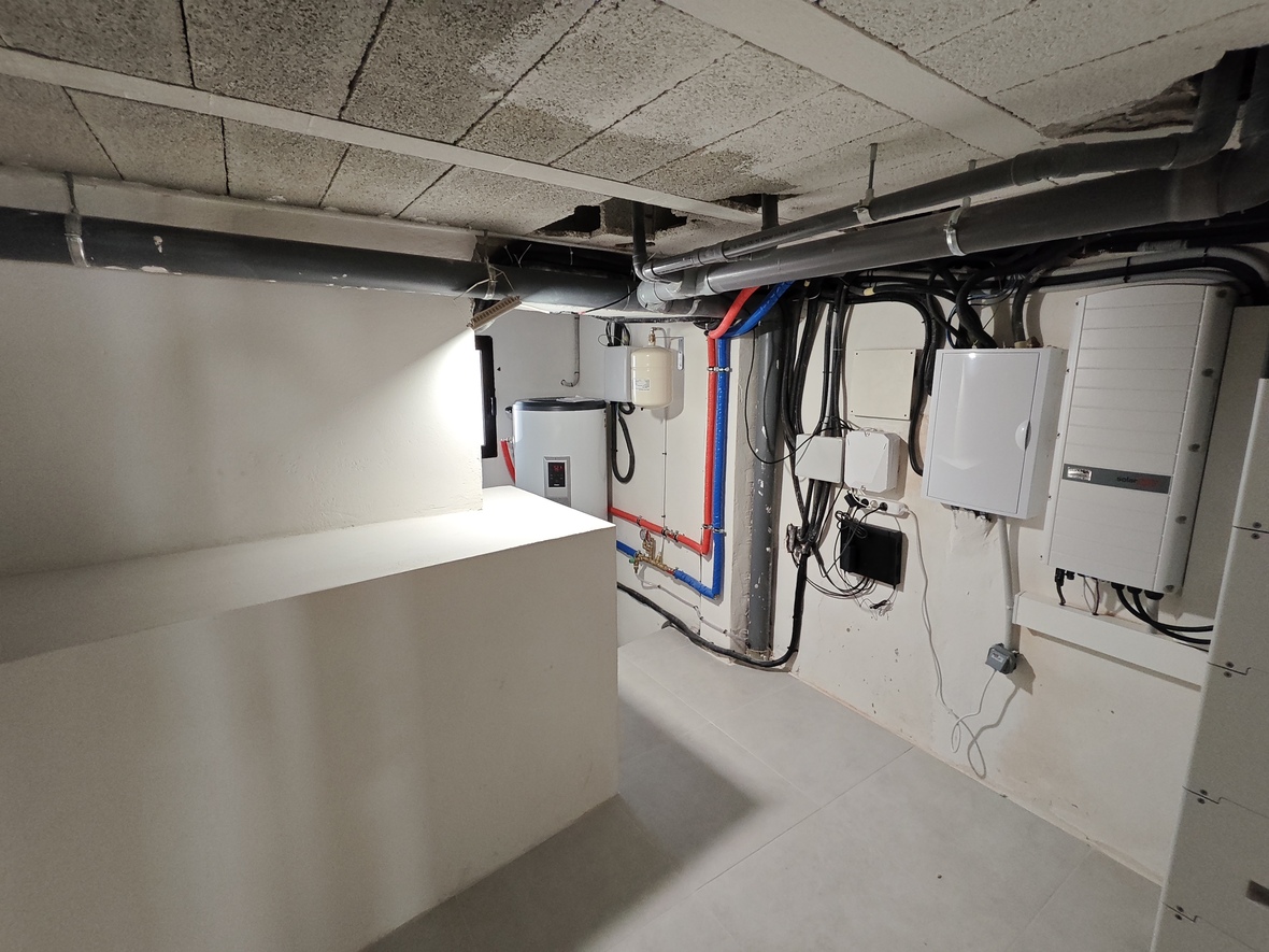 Cuarto técnico con inversor SolarEdge, cuadros eléctricos y sistema de agua caliente con tuberías PEX y desagües vistos bajo techo de bovedilla.