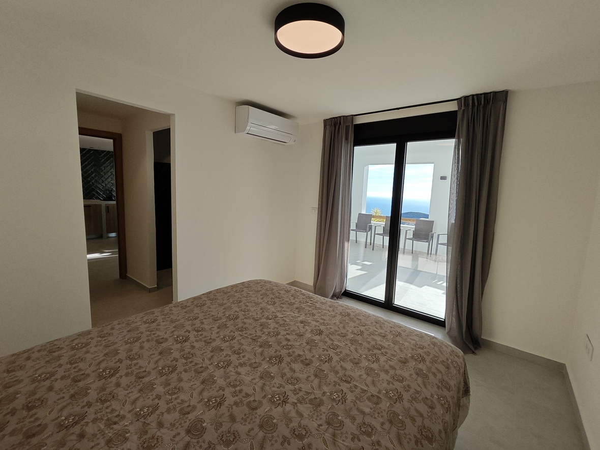 Dormitorio con acceso directo a una terraza con vistas al mar. Incluye aire acondicionado, tonos neutros y amplios ventanales correderos con cortinas grises.