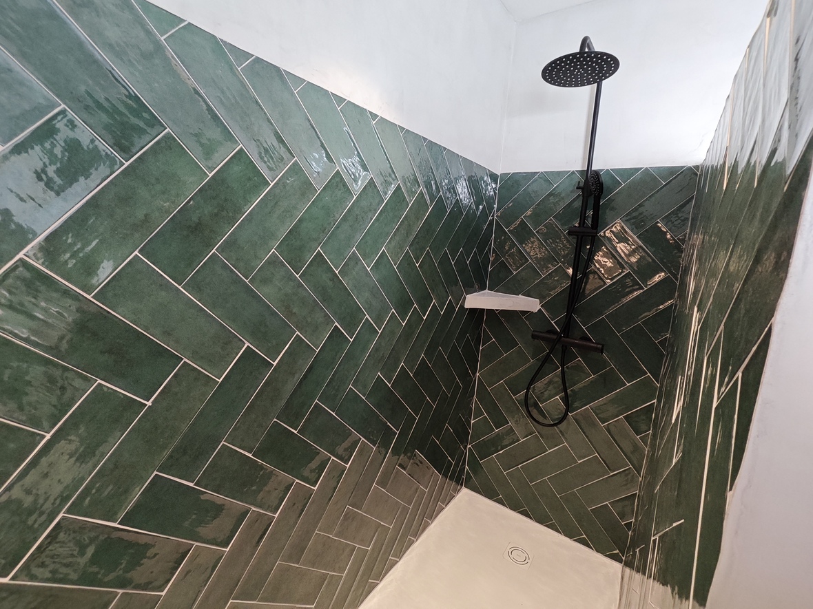Ducha con revestimiento de azulejos verdes brillantes en espiga, equipada con grifería negra de diseño y plato de ducha blanco.