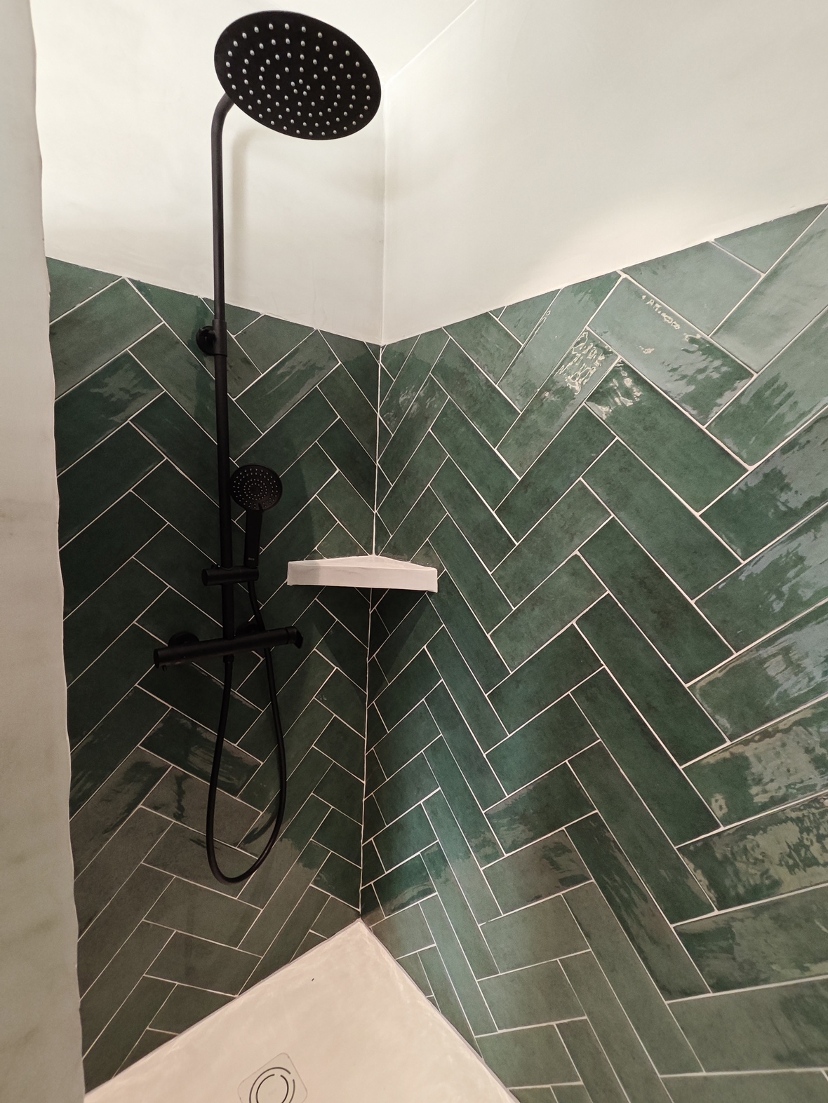 Ducha moderna con azulejos verde esmeralda dispuestos en espiga, grifería en negro mate y un amplio rociador de efecto lluvia.