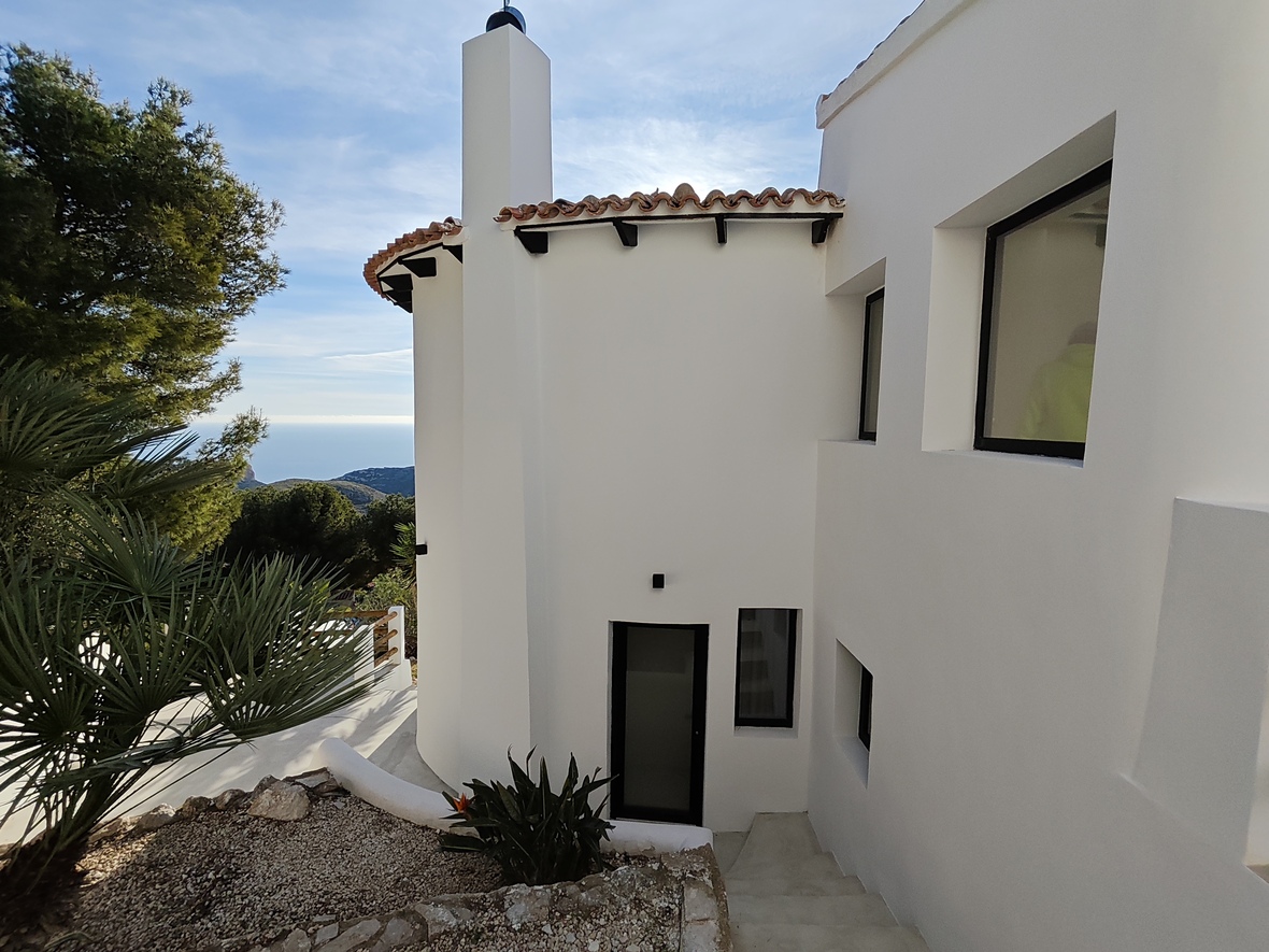 Exterior de villa mediterránea con fachada blanca, tejado de teja cerámica y escaleras de acceso que ofrecen vistas panorámicas al mar y la montaña.