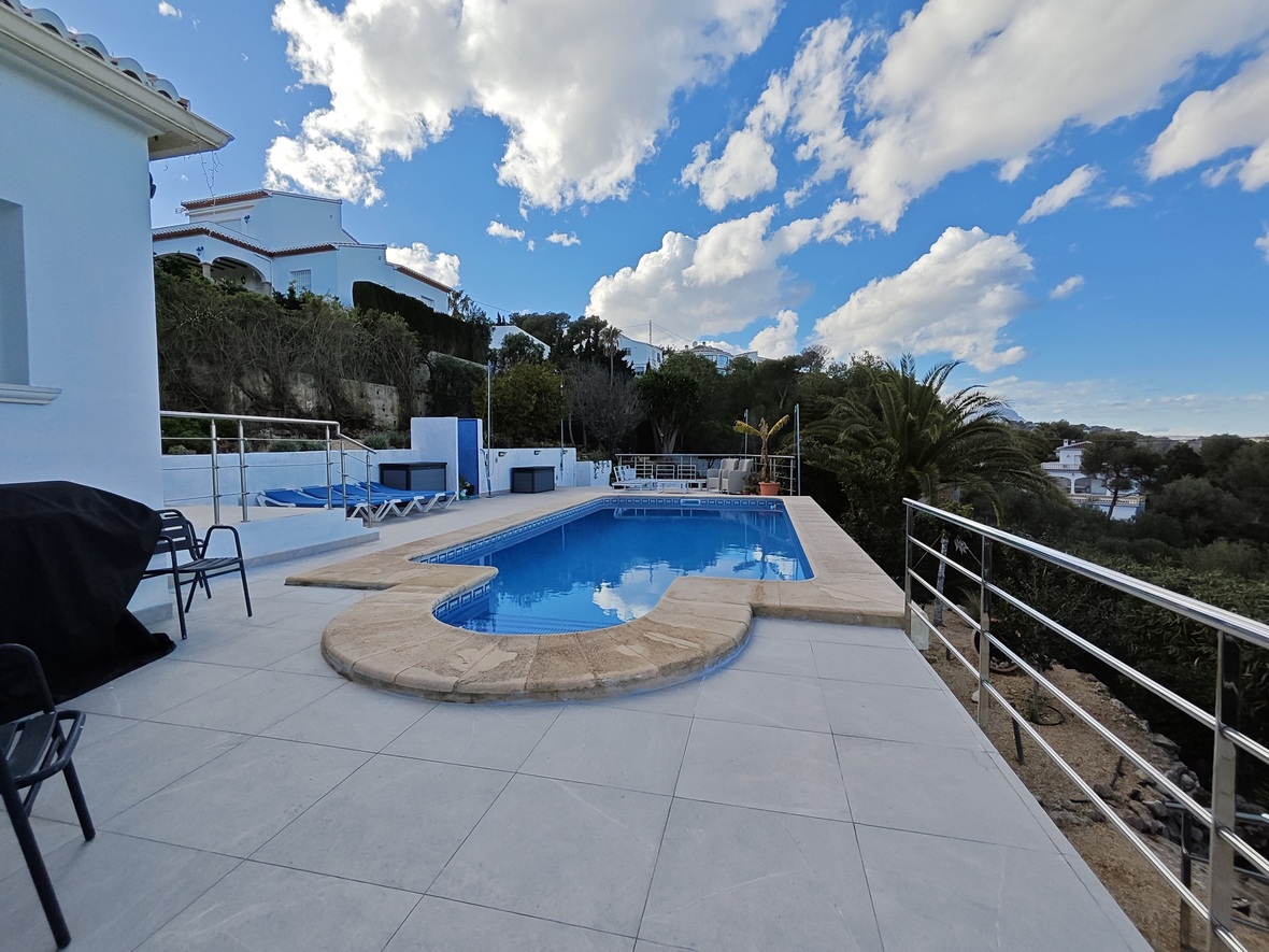 Piscina exterior con borde de piedra, rodeada de una amplia terraza de gres y barandillas de acero inoxidable con vistas al entorno natural.