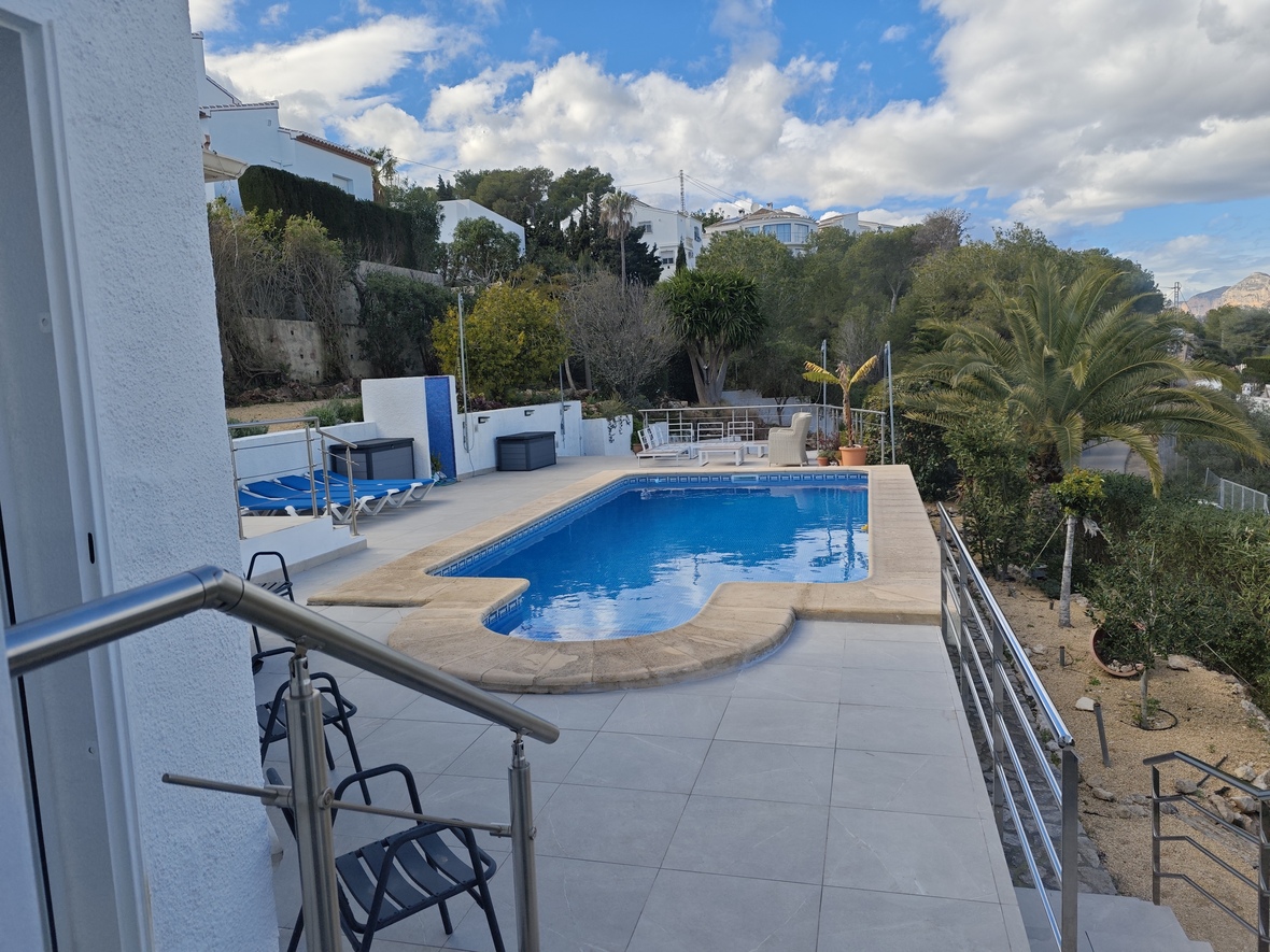 Piscina exterior con escaleras romanas, rodeada de una terraza de gres porcelánico, barandillas de acero inoxidable y vegetación mediterránea.