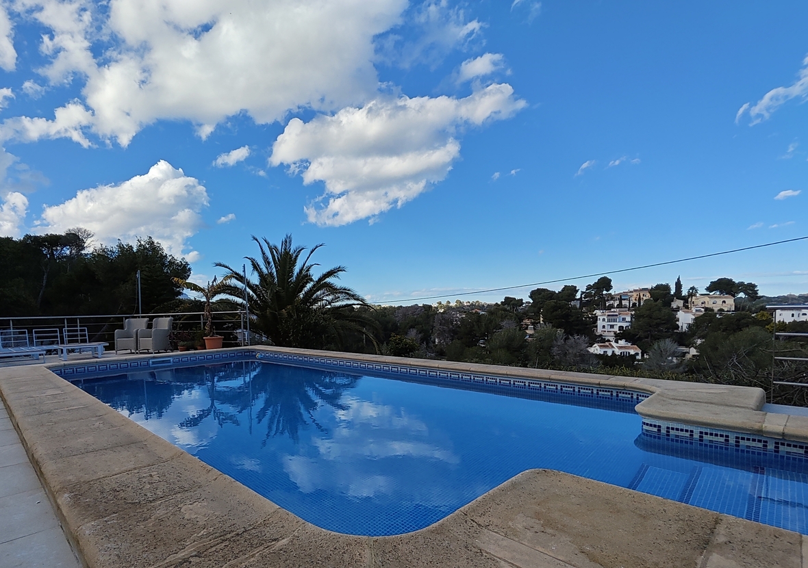 Piscina exterior con revestimiento de gresite azul y borde de piedra, con vistas despejadas al entorno residencial mediterráneo y vegetación local.