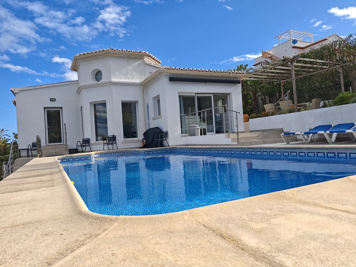 Piscina privada con azulejos azules, rodeada por una terraza de piedra y una villa blanca con un distintivo torreón circular y ventanales.