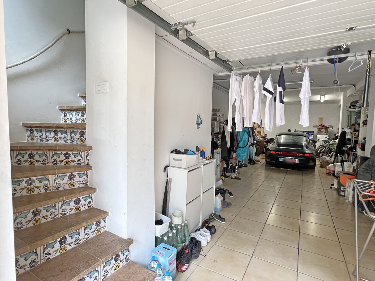 Amplio garaje con suelo cerámico y zona de almacenaje, que incluye una escalera interior decorada con azulejos tradicionales para acceder a la vivienda.