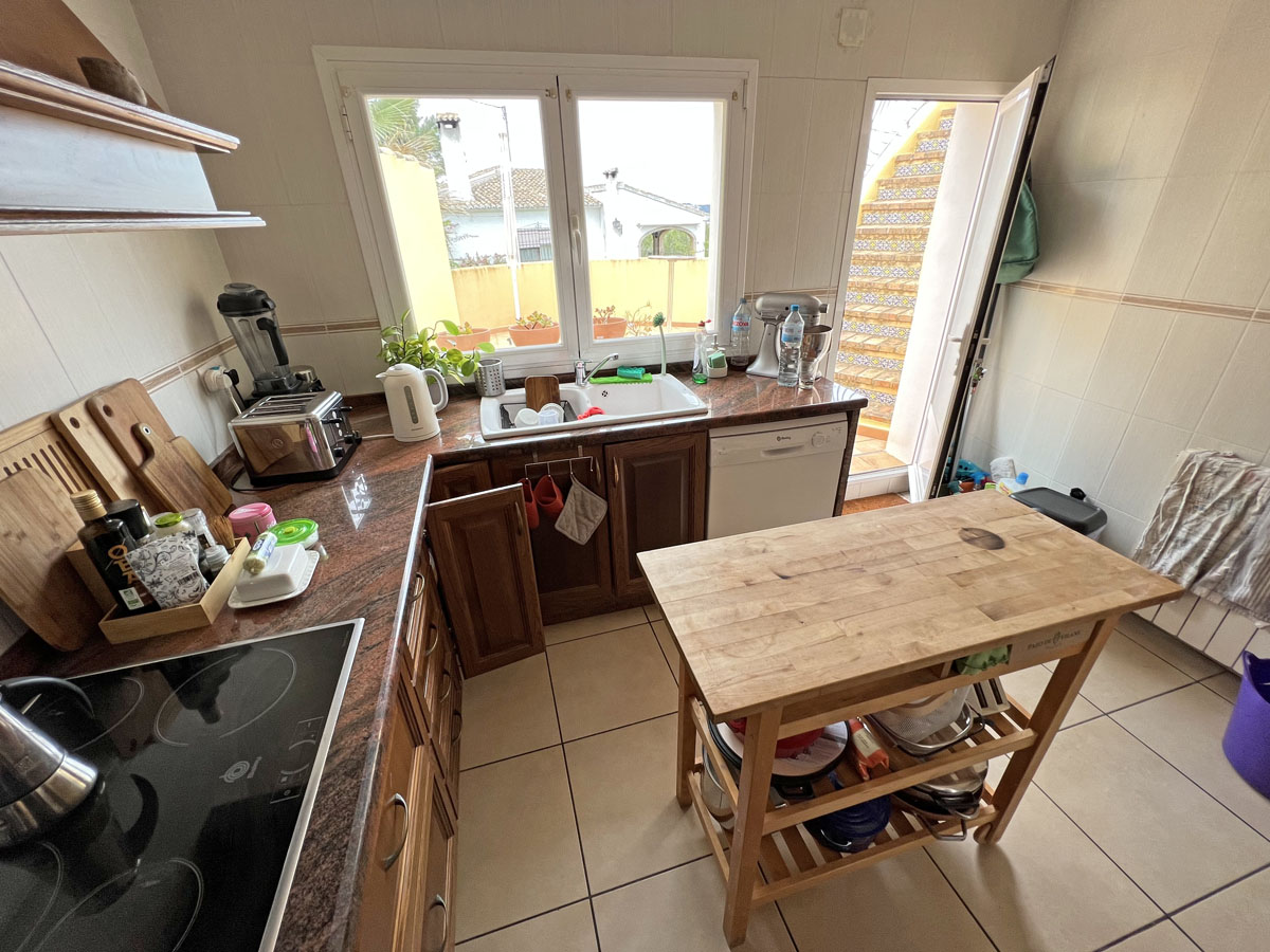 Cocina independiente con encimeras de granito, armarios de madera y una isla auxiliar. Incluye acceso directo a una escalera exterior con azulejos tradicionales.