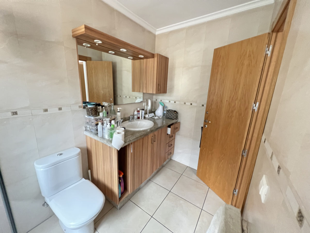 Cuarto de baño con mueble de madera, encimera de piedra y lavabo integrado. Incluye paredes alicatadas en tonos crema y un espejo con iluminación superior.