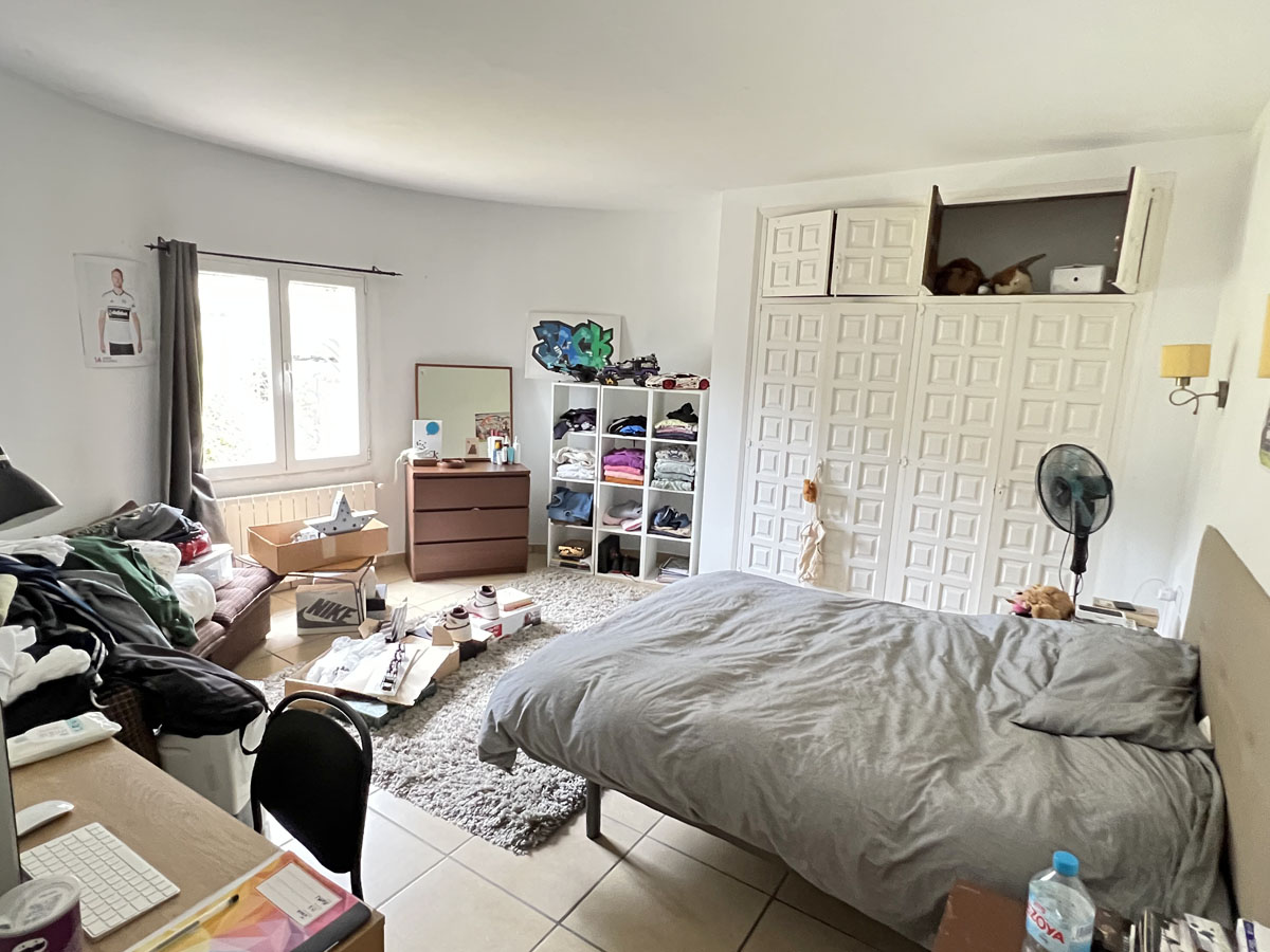 Dormitorio con amplios armarios empotrados de diseño tradicional blanco, suelos cerámicos y ventana exterior que aporta luz natural.