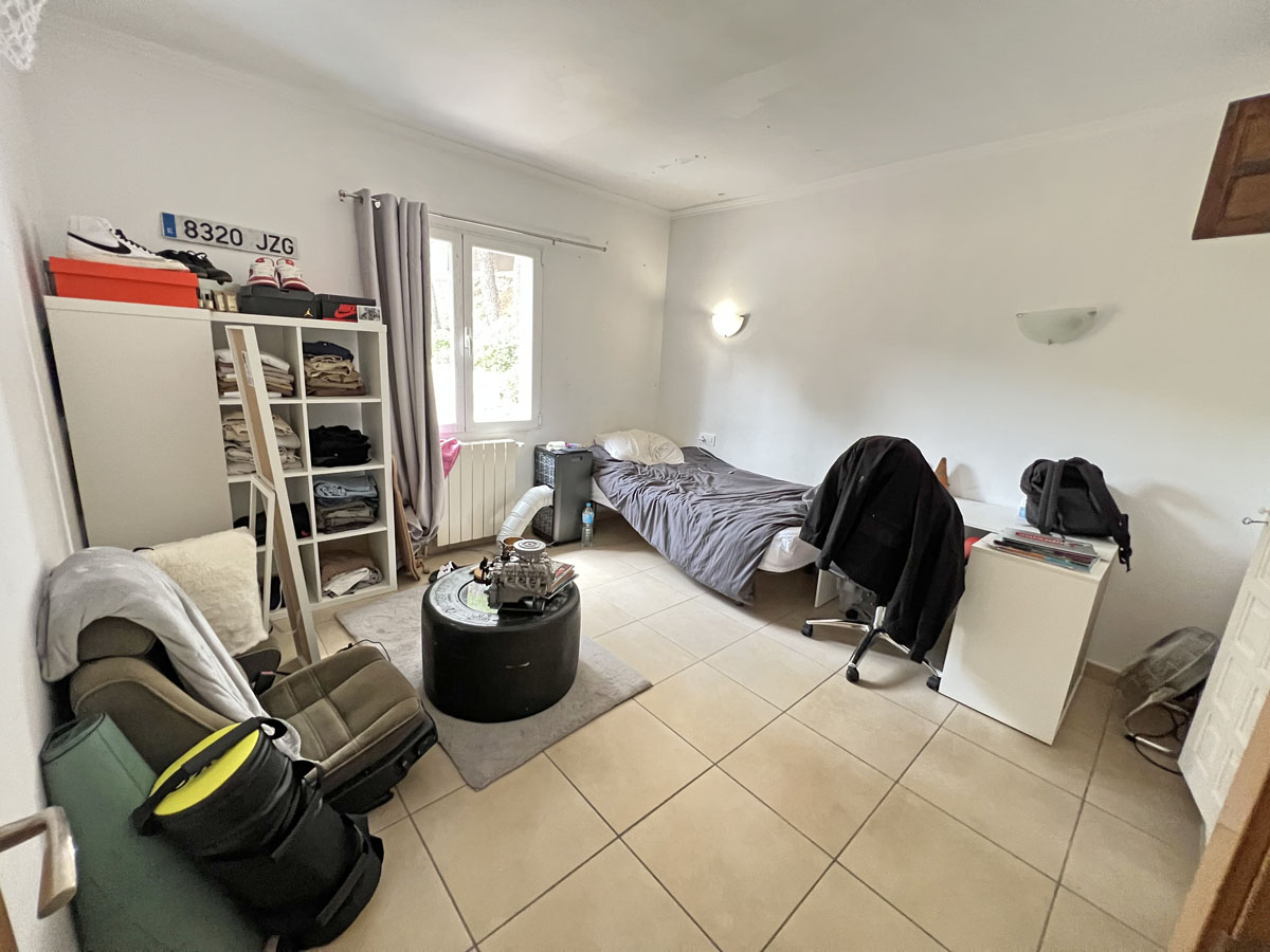 Dormitorio funcional con suelos de gres, ventana de PVC blanca y radiador. El espacio cuenta con iluminación natural y paredes en tonos neutros.