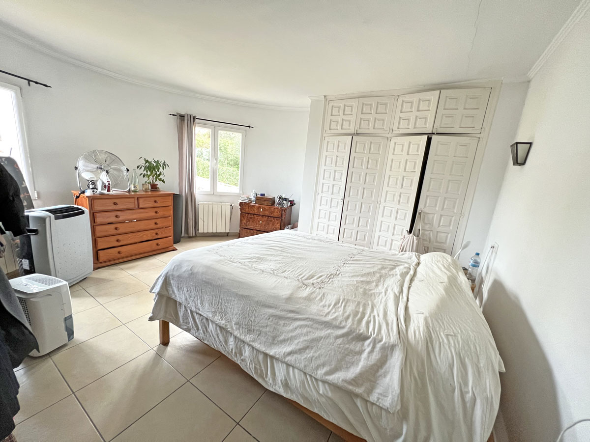 Dormitorio luminoso con amplios armarios empotrados de estilo tradicional, suelos de gres y mobiliario de madera natural bajo una suave luz exterior.