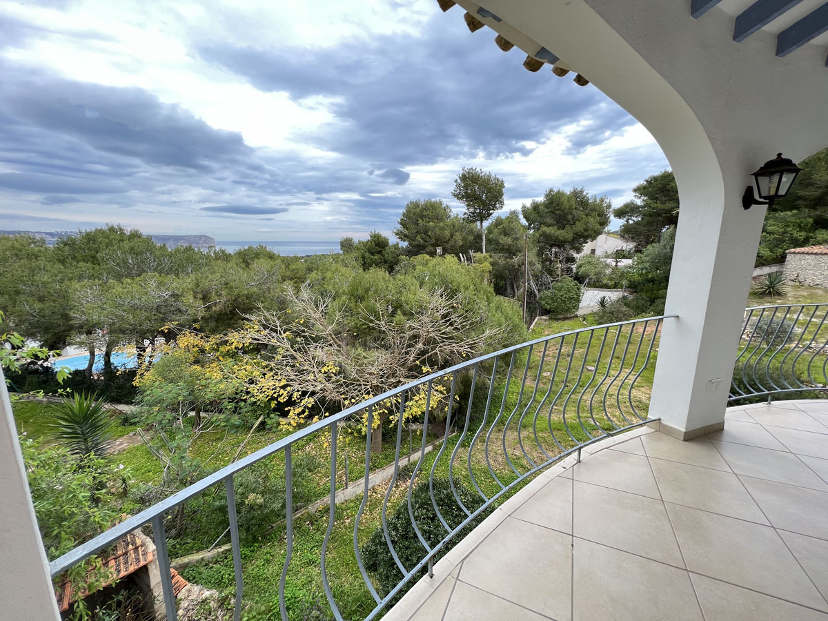 Terraza cubierta con suelos cerámicos y barandilla de hierro, ofreciendo vistas panorámicas al mar Mediterráneo y al Cabo San Antonio entre pinos.