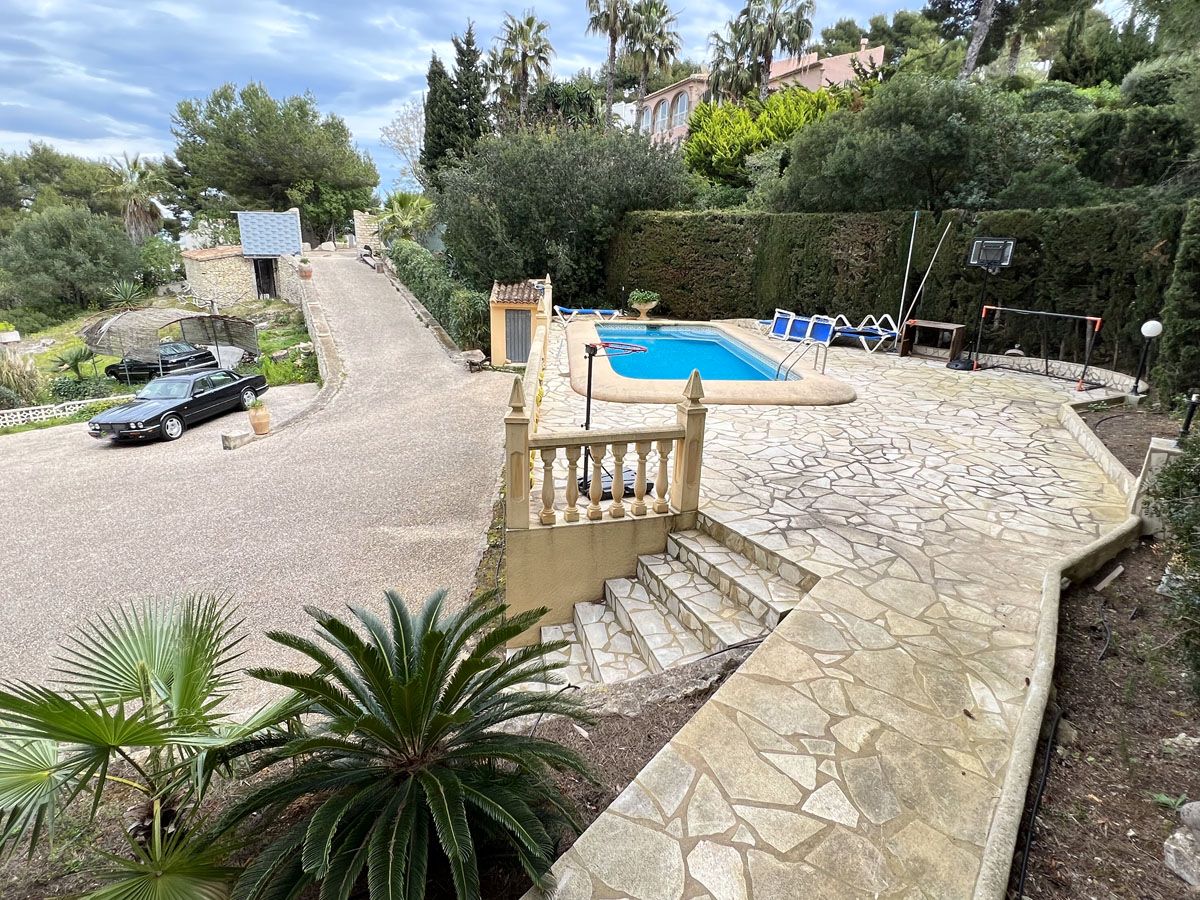 Terraza elevada con pavimento de piedra natural, piscina privada y amplia zona de aparcamiento rodeada de vegetación mediterránea madura.