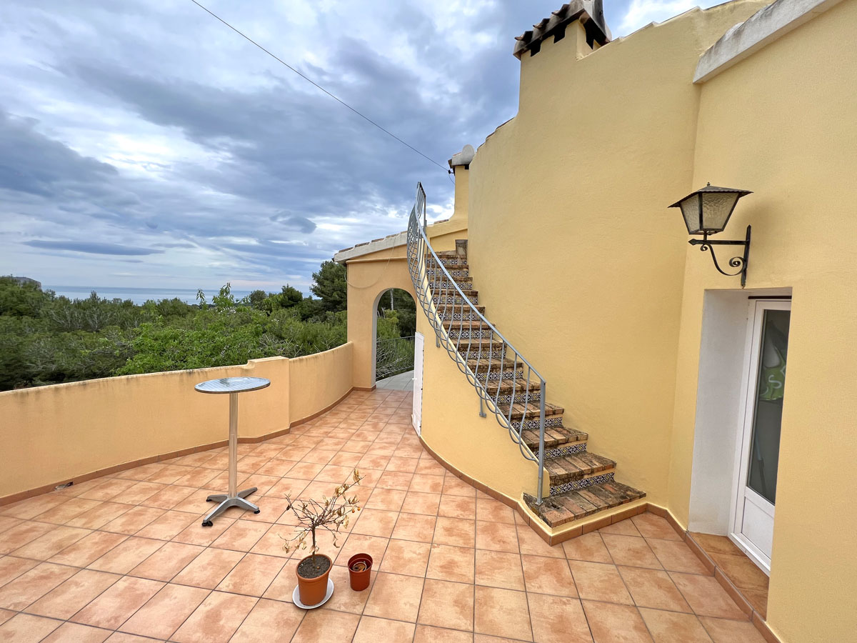 Terraza exterior con suelos de terracota y una escalera curva decorada con azulejos tradicionales. Ofrece vistas panorámicas al mar y al entorno natural de Jávea.
