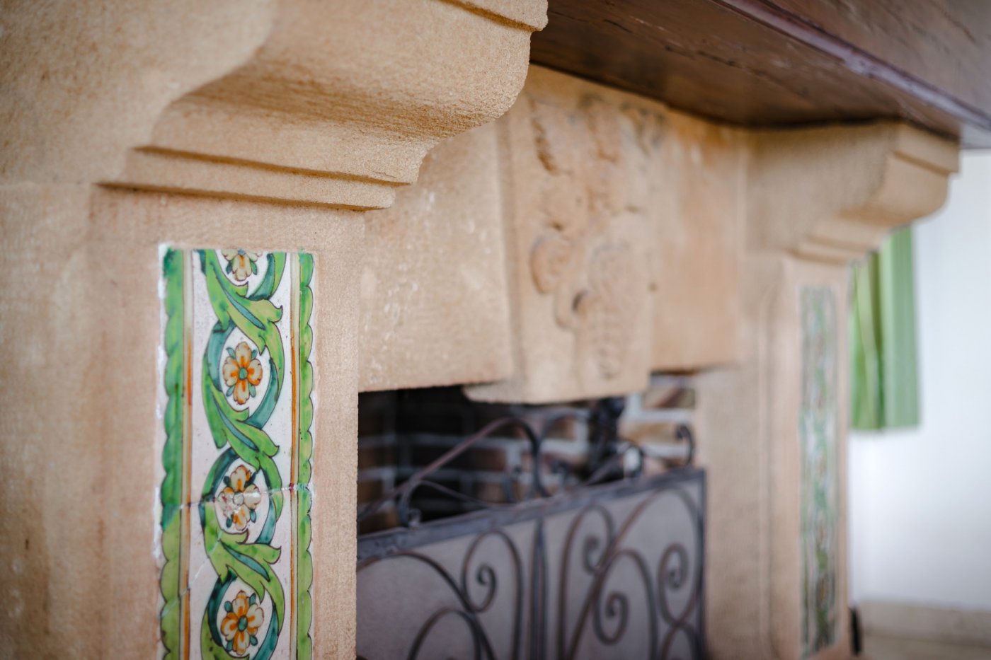 Detalle de chimenea de piedra tosca con azulejos artesanales pintados a mano, relieves tallados y repisa de madera maciza.