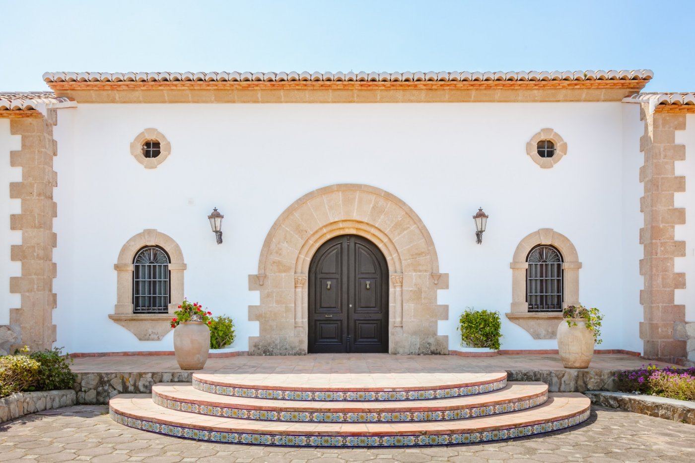 Entrada principal con arco de piedra tosca, puertas de madera oscura y escalones semicirculares decorados con azulejos tradicionales.