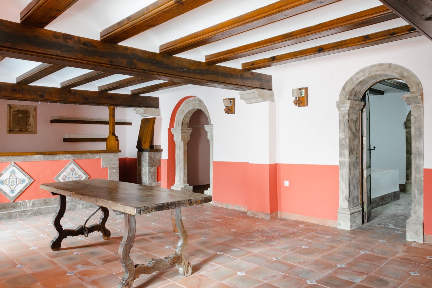 Espaciosa estancia tradicional con vigas de madera vista, suelos de barro cocido y arcos de piedra tosca tallada que conectan con otras salas de la propiedad.
