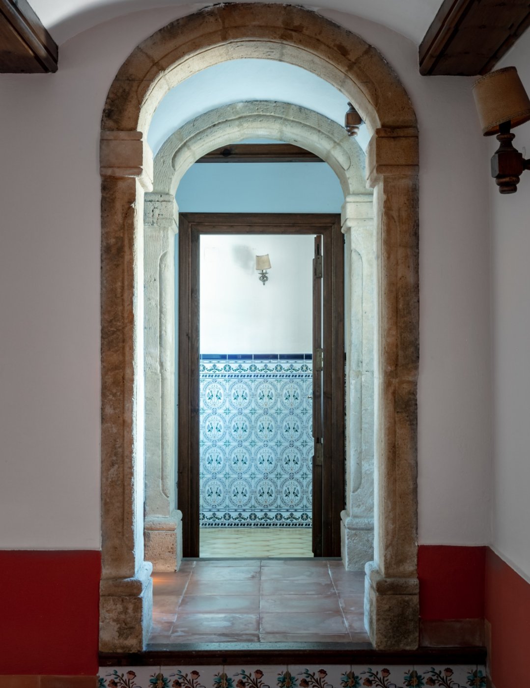 Pasillo con arcos tradicionales de piedra tosca que conducen a una estancia con azulejos decorativos y suelos de terracota.