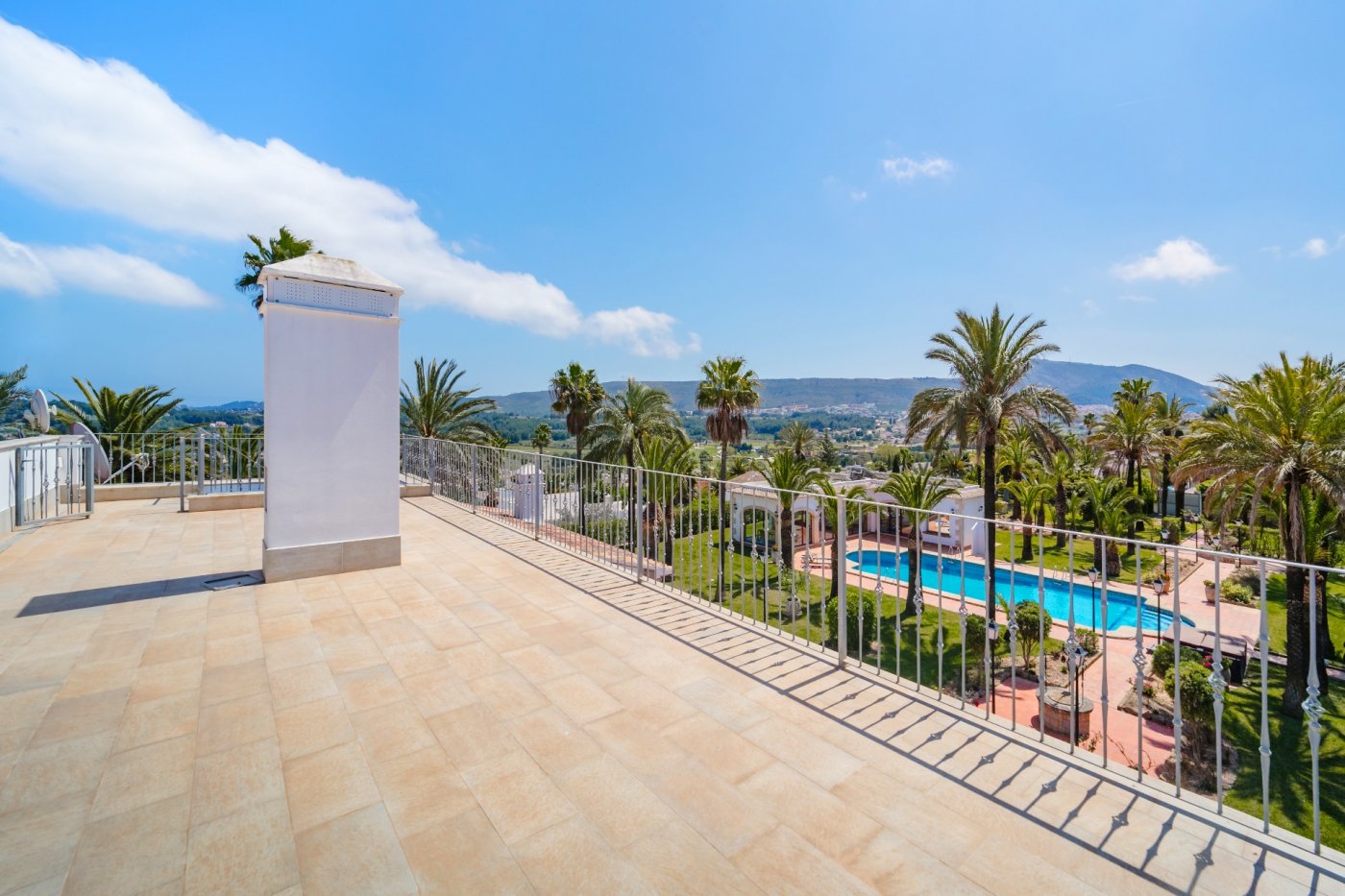 Terraza superior con suelo cerámico y barandilla metálica, ofreciendo vistas panorámicas al jardín de palmeras, la piscina de 16x7 metros y el valle circundante.