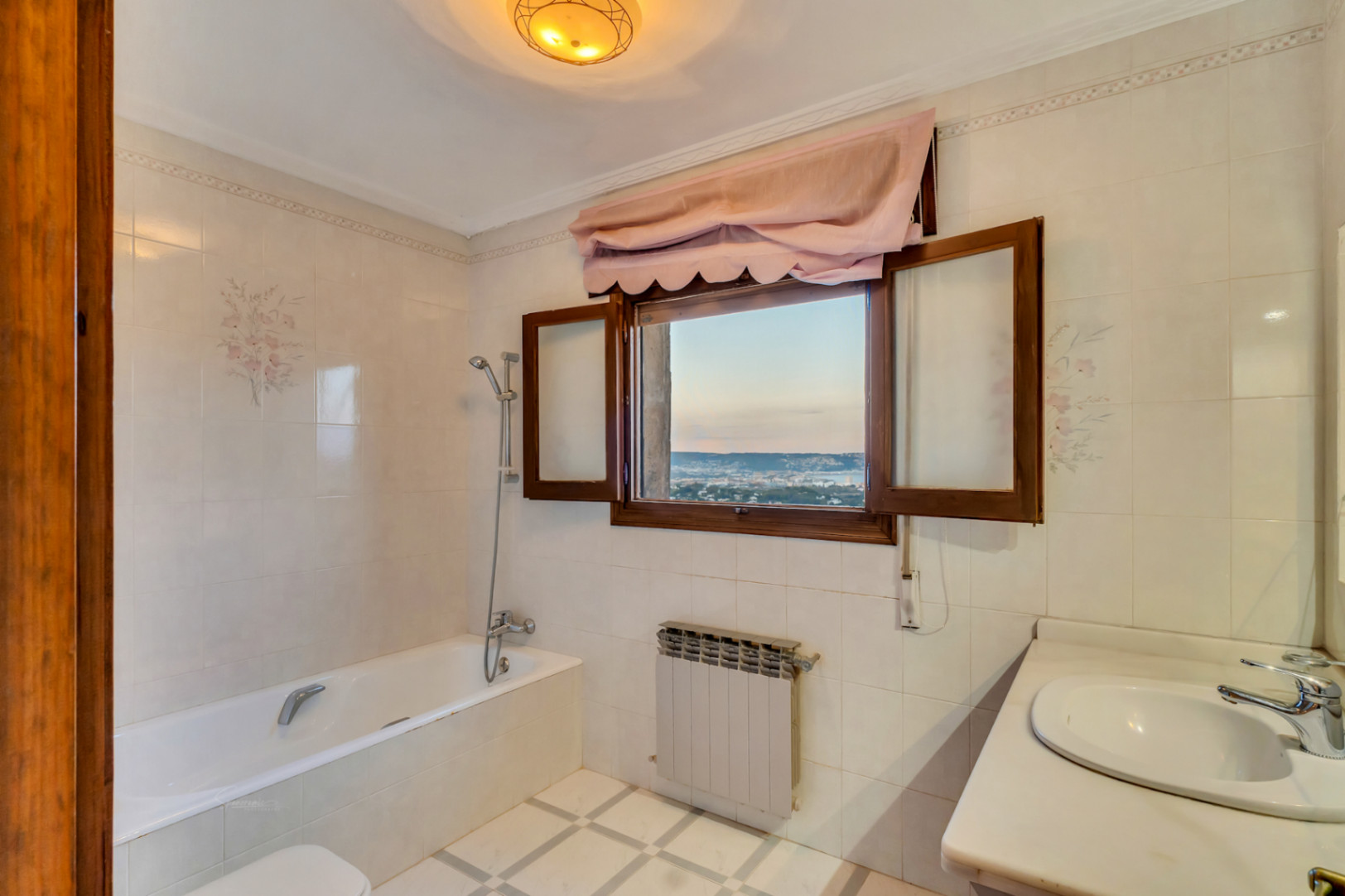 Baño con bañera y encimera de mármol, destacando una ventana de madera que ofrece vistas panorámicas a la bahía de Jávea y luz natural.