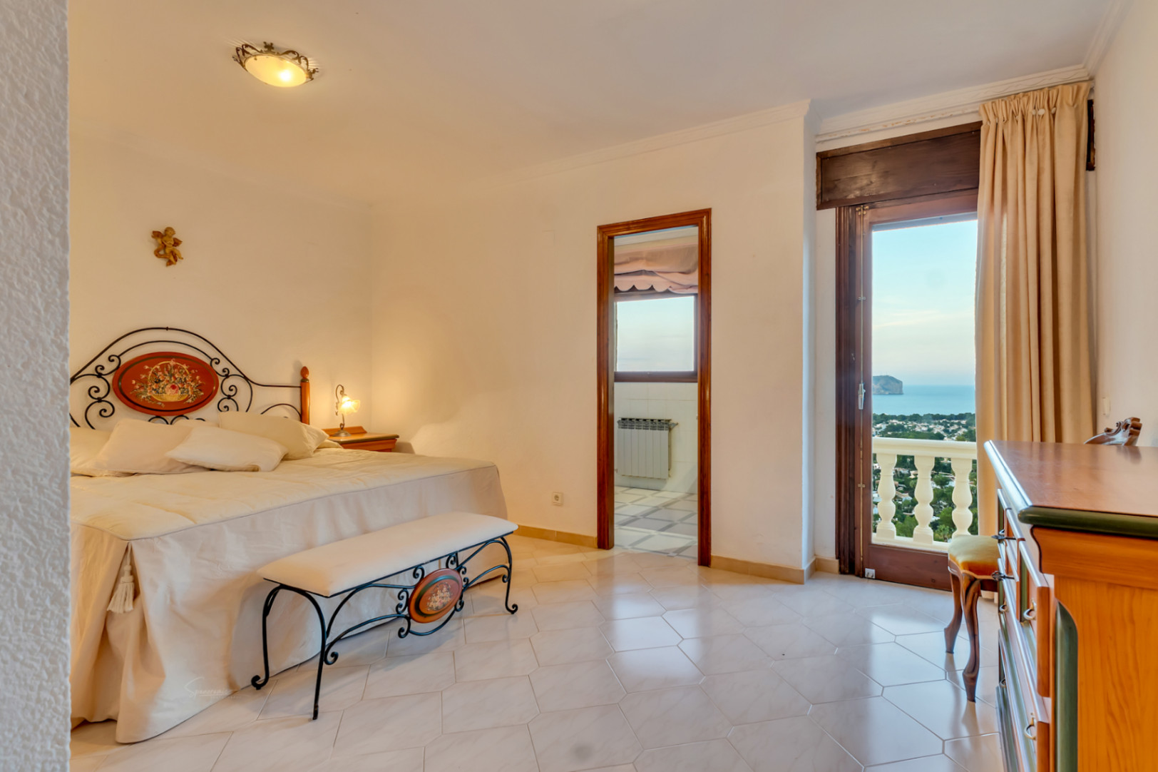 Dormitorio con cabecero de forja decorativa, suelos cerámicos y acceso directo a una terraza con vistas panorámicas al mar y al Cabo San Antonio.