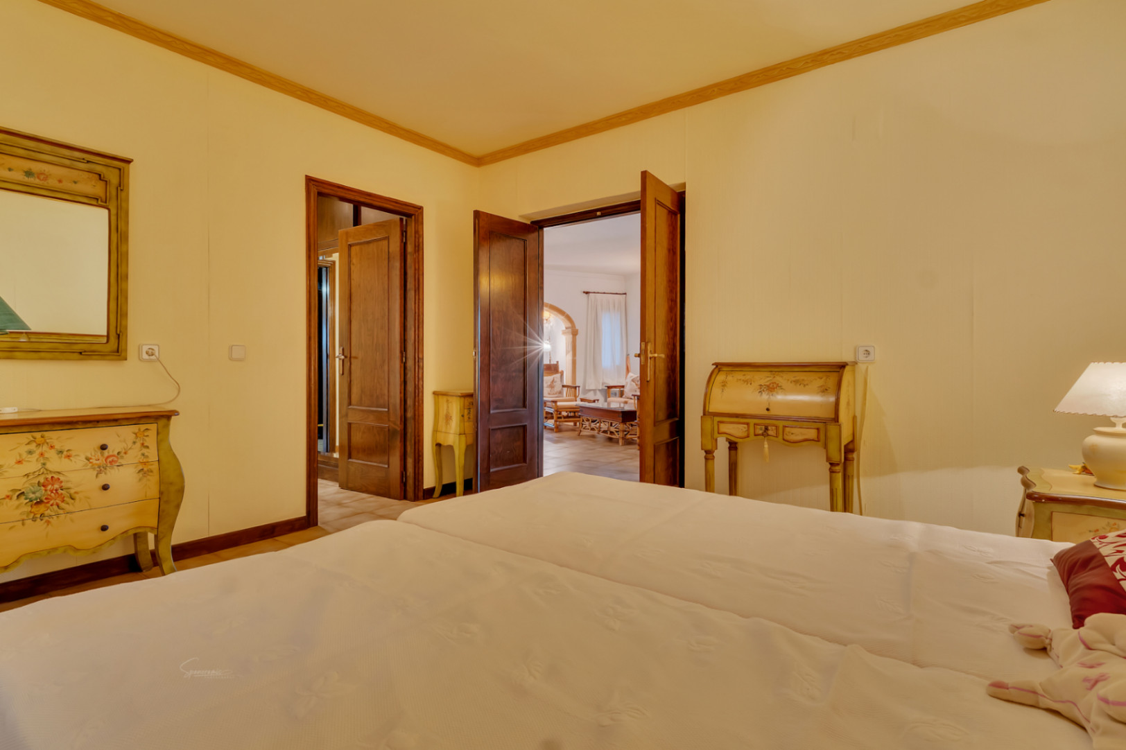 Dormitorio con mobiliario de estilo clásico pintado a mano, puertas de madera maciza y acceso directo al salón principal a través de un arco de piedra.