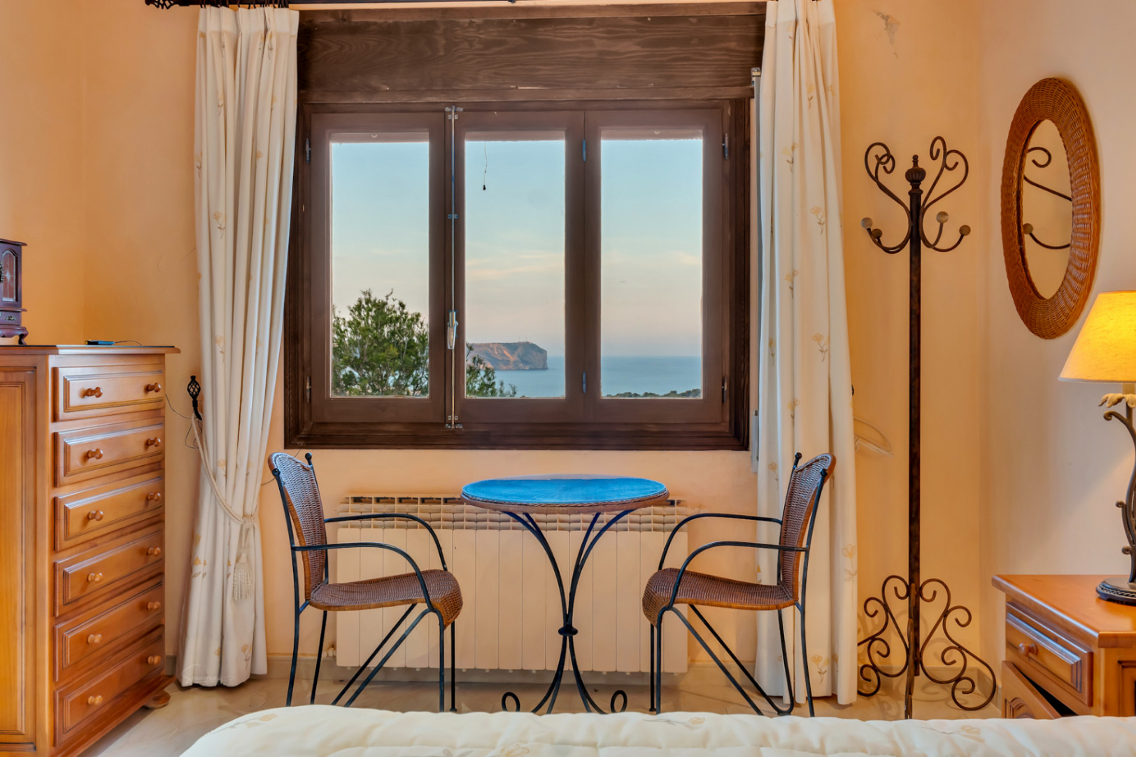 Dormitorio con rincón de lectura, mobiliario de madera y vistas panorámicas al mar y al Cabo San Antonio a través de un gran ventanal.