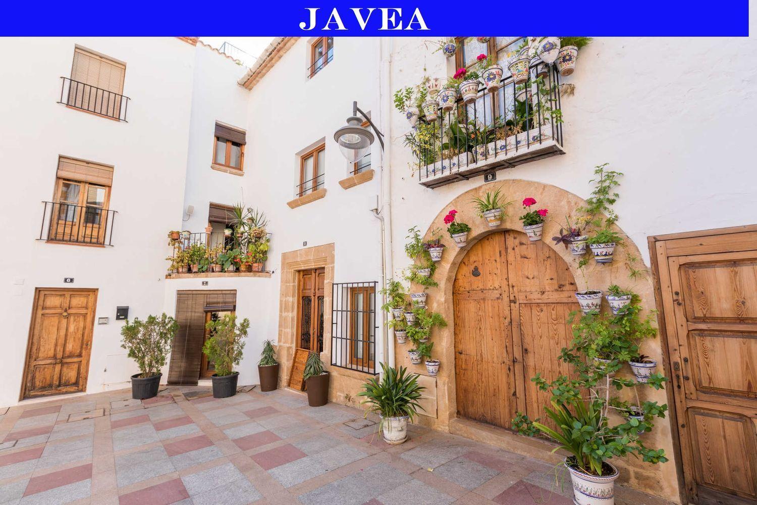 Fachada tradicional en el centro histórico de Jávea con puertas de madera, arcos de piedra tosca y macetas de cerámica decorativas sobre paredes blancas.