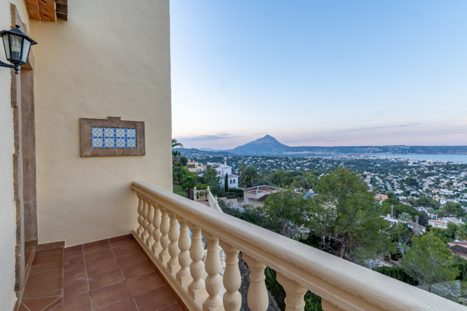 Terraza con suelo de terracota y balaustrada clásica que ofrece vistas panorámicas al Montgó y la bahía de Jávea. Destaca el detalle decorativo de azulejos en la pared.