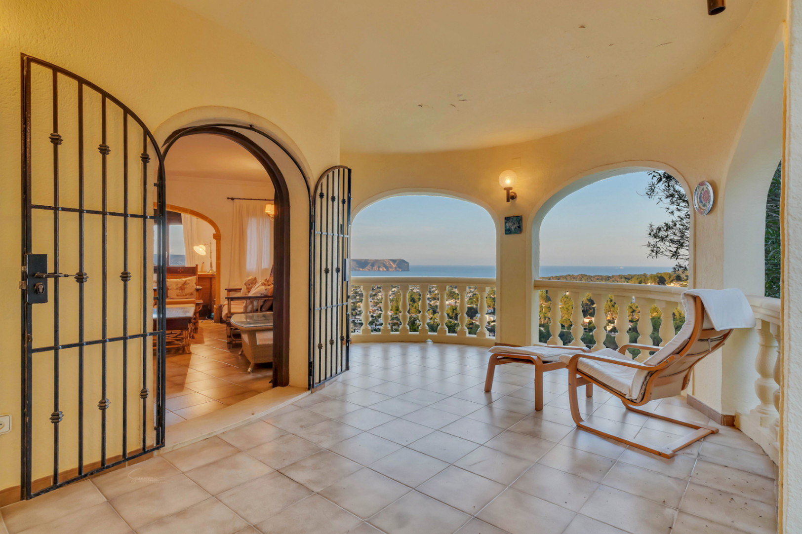 Terraza cubierta con arcos, suelo cerámico y vistas panorámicas al mar. Incluye acceso directo al salón mediante puertas de forja y balustrada clásica.