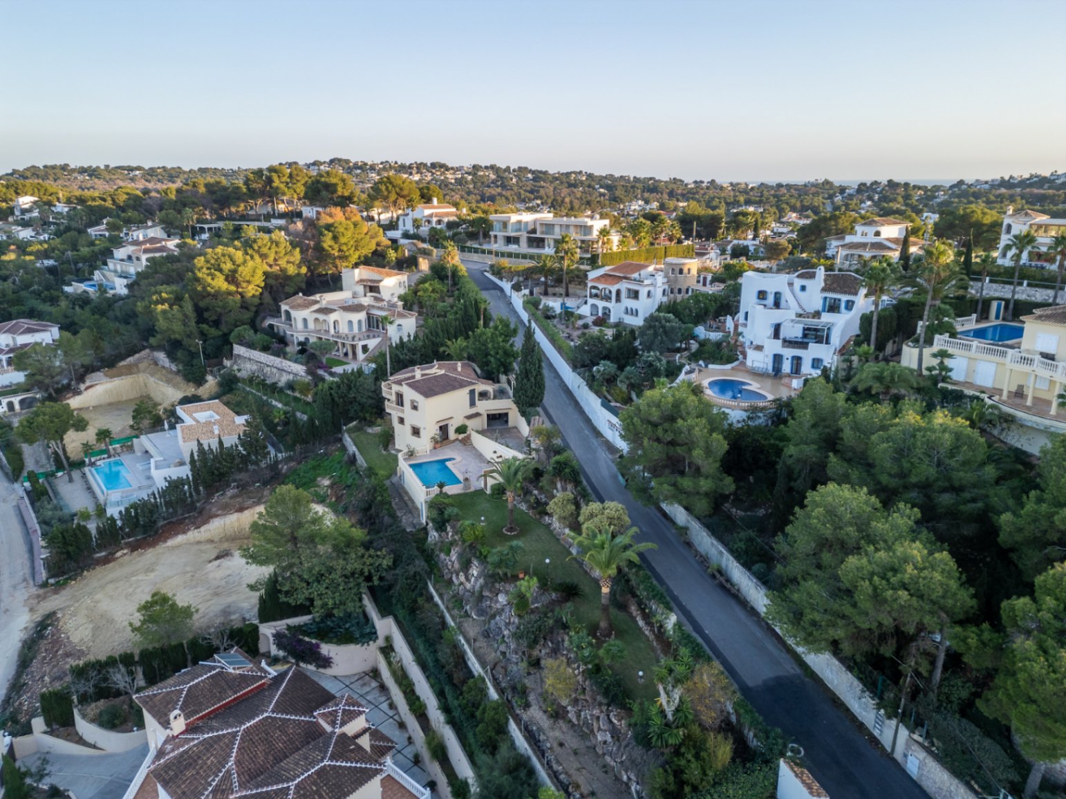 Vista aérea de la urbanización en Costa Nova Panorama, mostrando villas de estilo mediterráneo con piscinas privadas rodeadas de pinos y jardines cuidados.