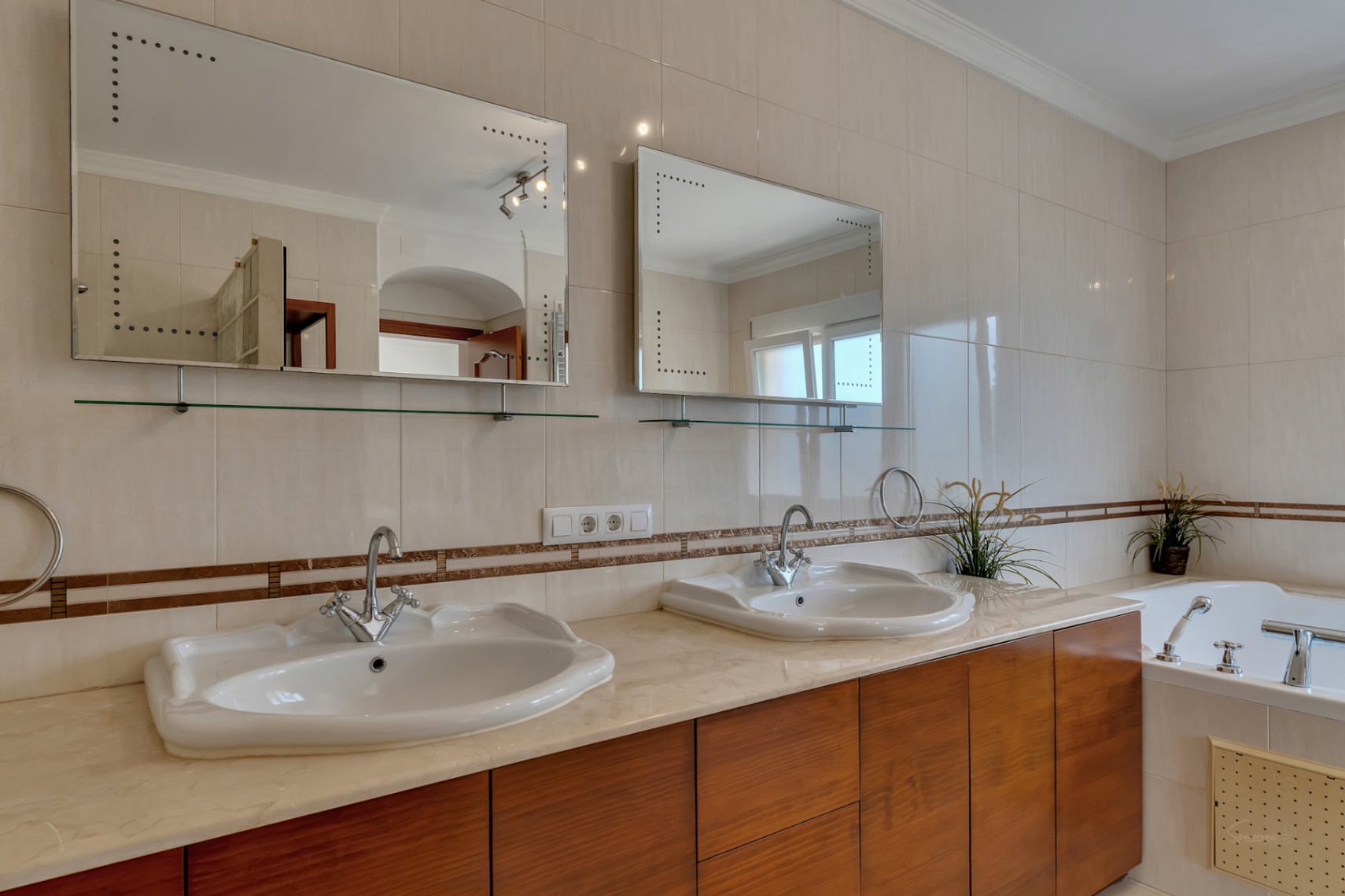Baño en suite con lavabo doble sobre encimera de mármol, muebles de madera y espejos retroiluminados junto a la bañera de hidromasaje.