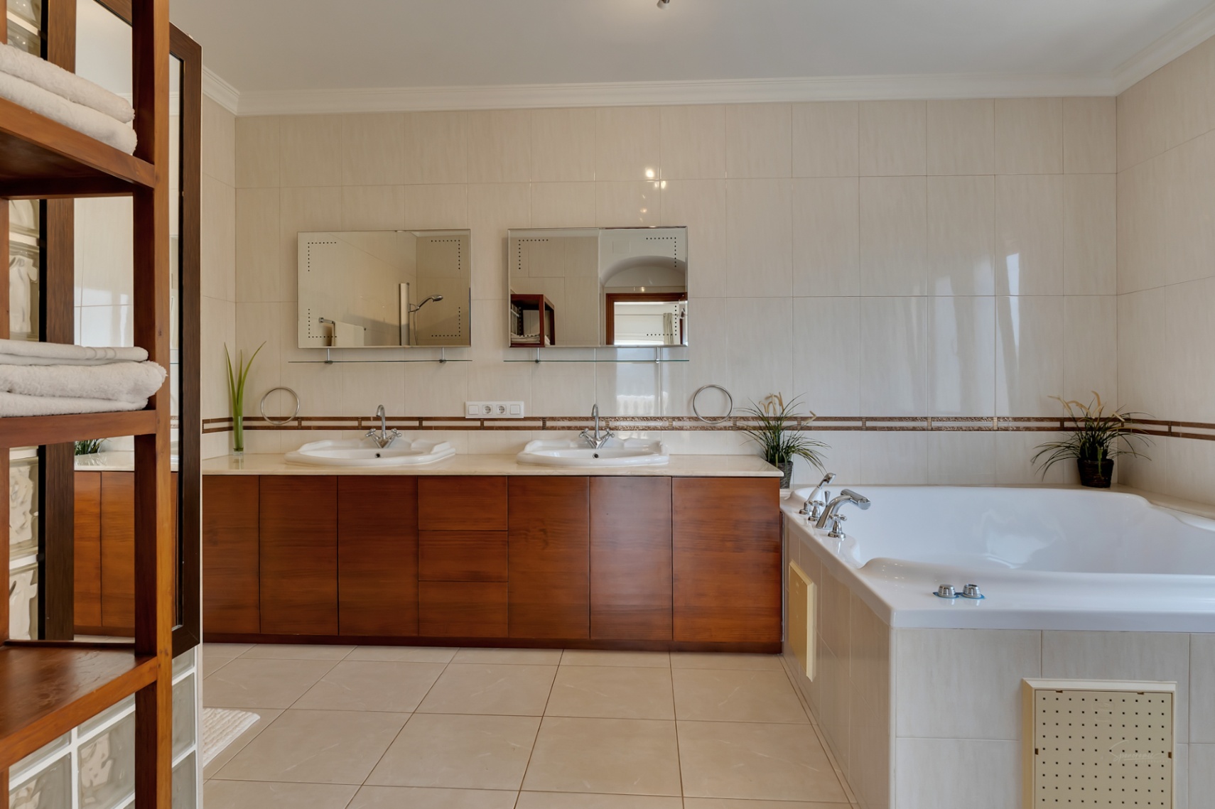 Baño principal con tocador doble de madera, amplia bañera de hidromasaje integrada y paredes revestidas en tonos crema con cenefas decorativas.