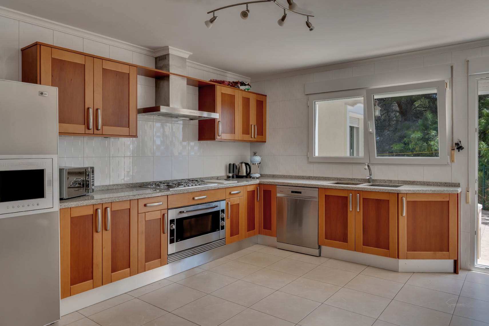 Cocina equipada con armarios de madera, encimera de granito, electrodomésticos de acero inoxidable y ventanal con luz natural.